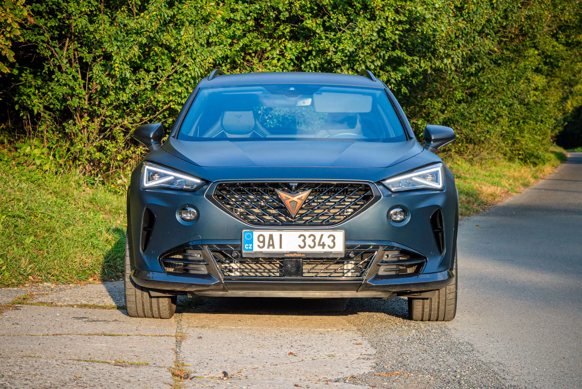Vue frontale moderne de la Cupra Formentor 2020 sur route pavée avec lumière naturelle du jour et arrière-plan rural, soulignant la grille agressive, les phares LED aiguisés, les contours dynamiques du capot et les caractéristiques de technologie avancée