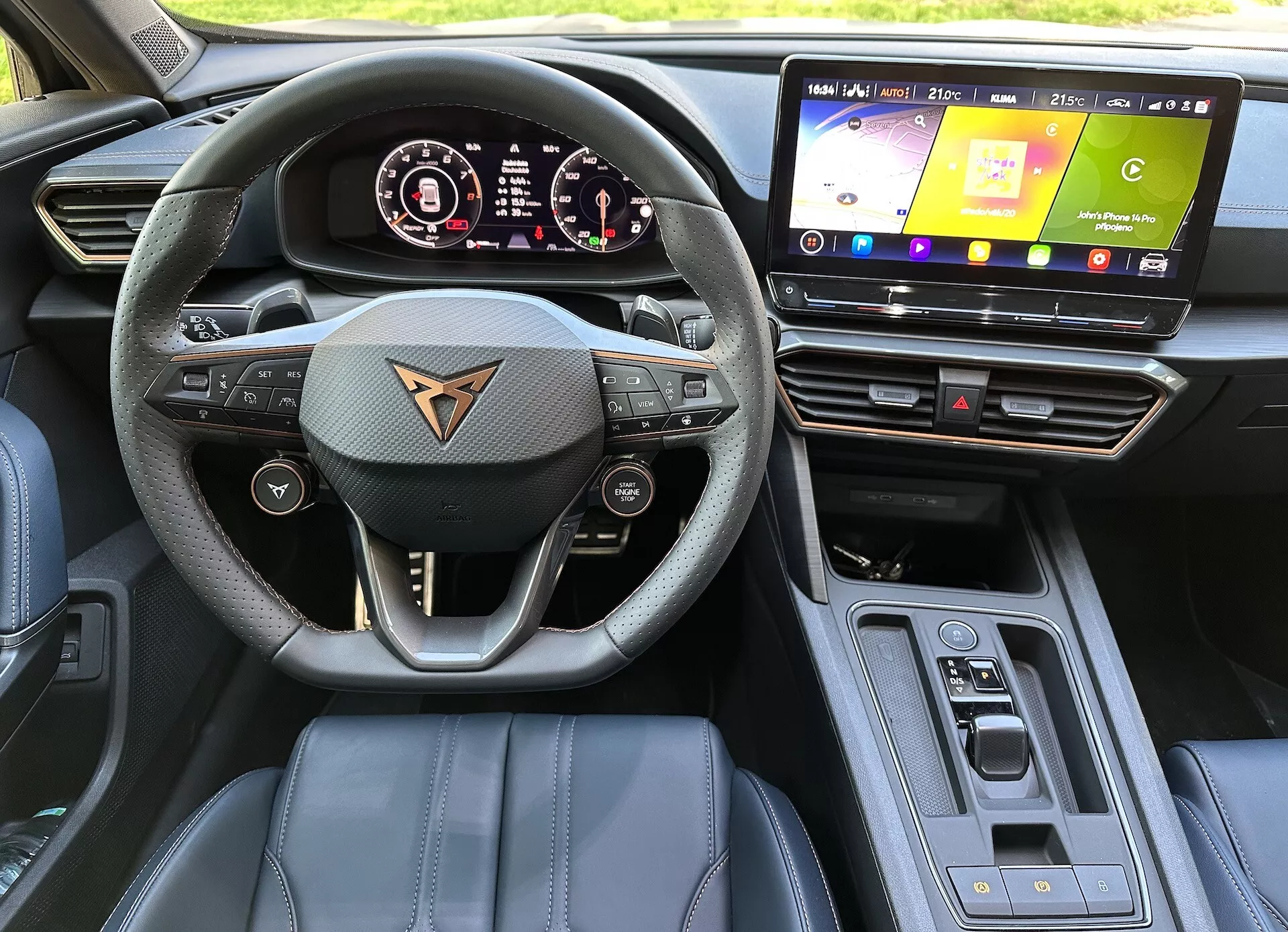 Vue intérieure de la Cupra Formentor 2020 du point de vue du conducteur montrant volant multifonctionnel en cuir avec le logo de la marque de la voiture, tableau de bord numérique, système d'infodivertissement tactile, matériaux du tableau de bord de haute qualité avec coutures accentuées, sélecteur de vitesse automatique, et fonctionnalités de haute technologie sous la lumière naturelle