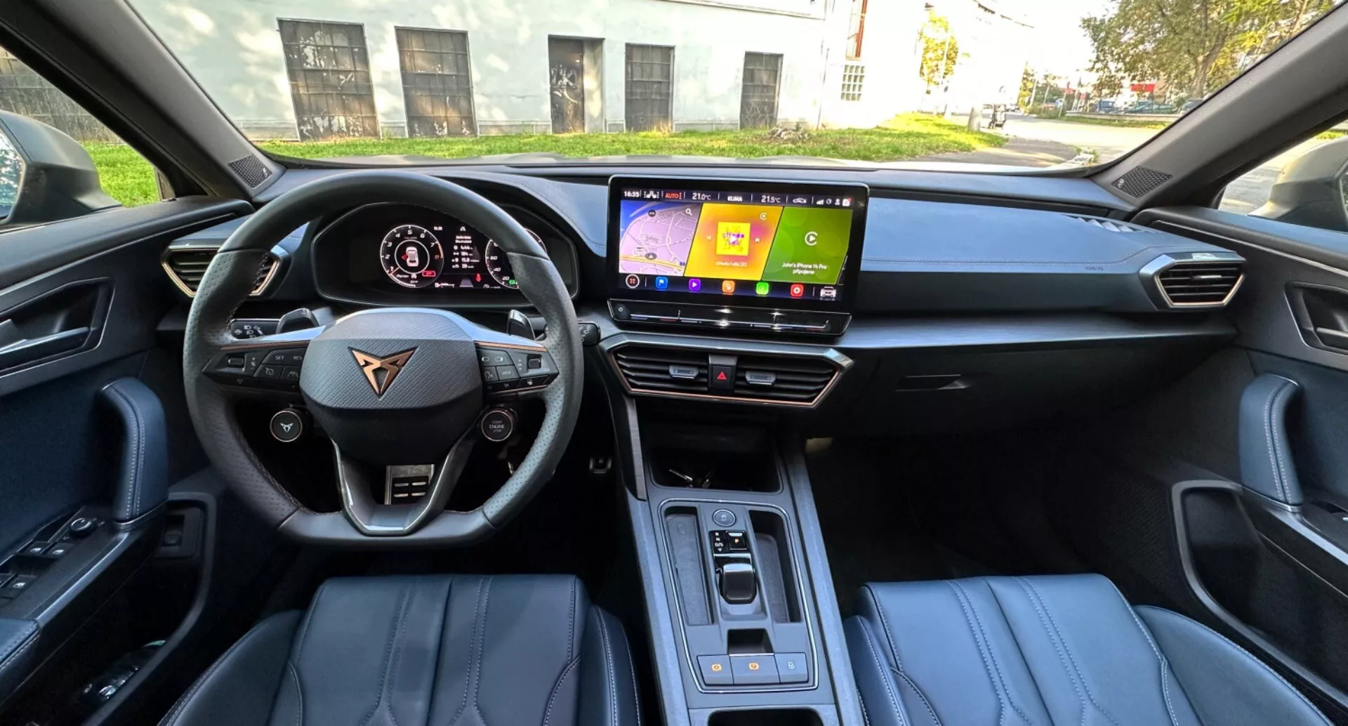 Vue intérieure d'un CUPRA Formentor 2020 depuis le siège du conducteur présentant un volant à fond plat avec boutons multimédia et régulateur de vitesse, un tableau de bord numérique affichant la vitesse et les tours par minute, un écran d'infodivertissement central, un sélecteur de vitesse automatique élégant, des sièges en cuir avec accent bicolore, et un éclairage de cabine en journée.