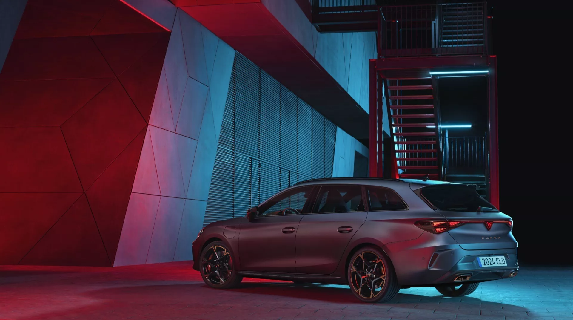 Cupra Leon 2024 première génération restylée photographiée sous un angle arrière trois quarts mettant en valeur le côté passager. L'éclairage nocturne dramatique met en évidence les caractéristiques de conception de la voiture, y compris les feux arrière sportifs, le pare-chocs arrière, l'aileron de toit agressif et les jantes axées sur les performances dans un cadre urbain industriel.