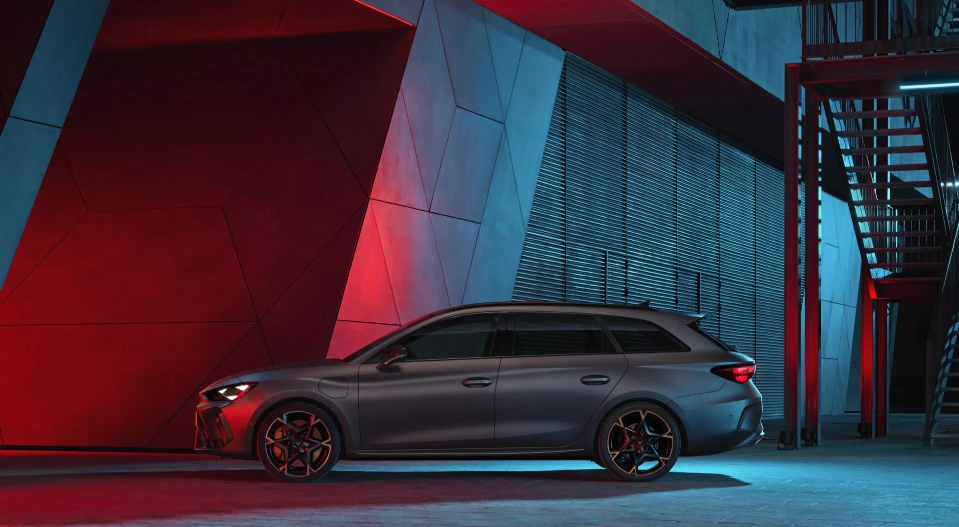Vue de profil latéral de la voiture sportive et élégante Cupra Leon 2024 en environnement urbain nocturne avec éclairage artificiel rouge et bleu en arrière-plan. La voiture présente une silhouette longue et aérodynamique avec des vitres teintées et des garnitures chromées, une ligne de toit se terminant par un aileron et des jantes en alliage à plusieurs rayons distinctifs. Les étriers de frein visibles suggèrent des freins axés sur les performances. La carrosserie a des lignes profilées et aucun badge ou caractéristique technologique n'est facilement identifiable sous cet angle.