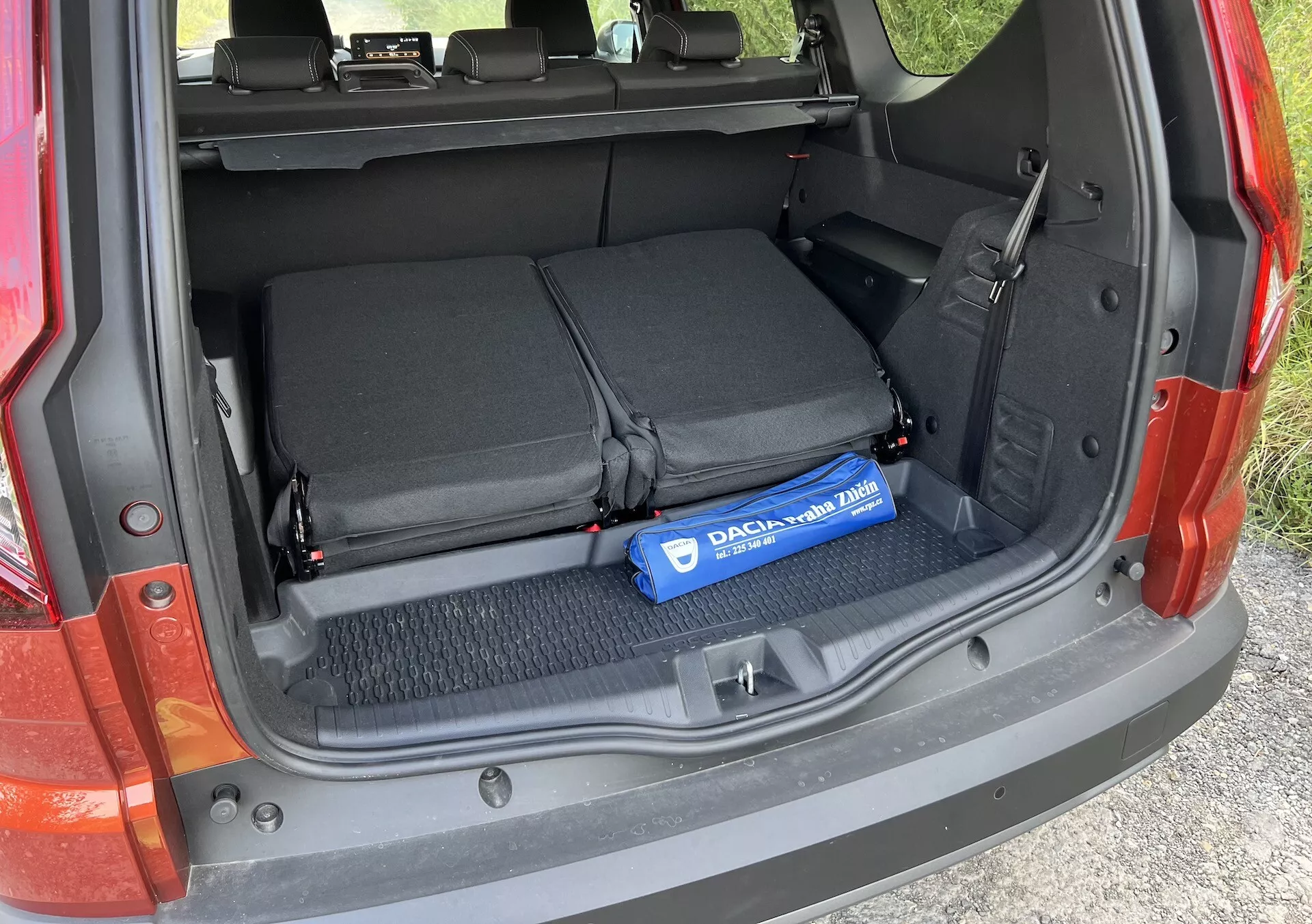 Détail du coffre de la Dacia Jogger 2022 montrant l'espace de chargement ouvert avec les sièges arrière rabattus, des boucles textiles pour sécuriser les objets, et un cylindre bleu Decaux sur le sol moquetté
