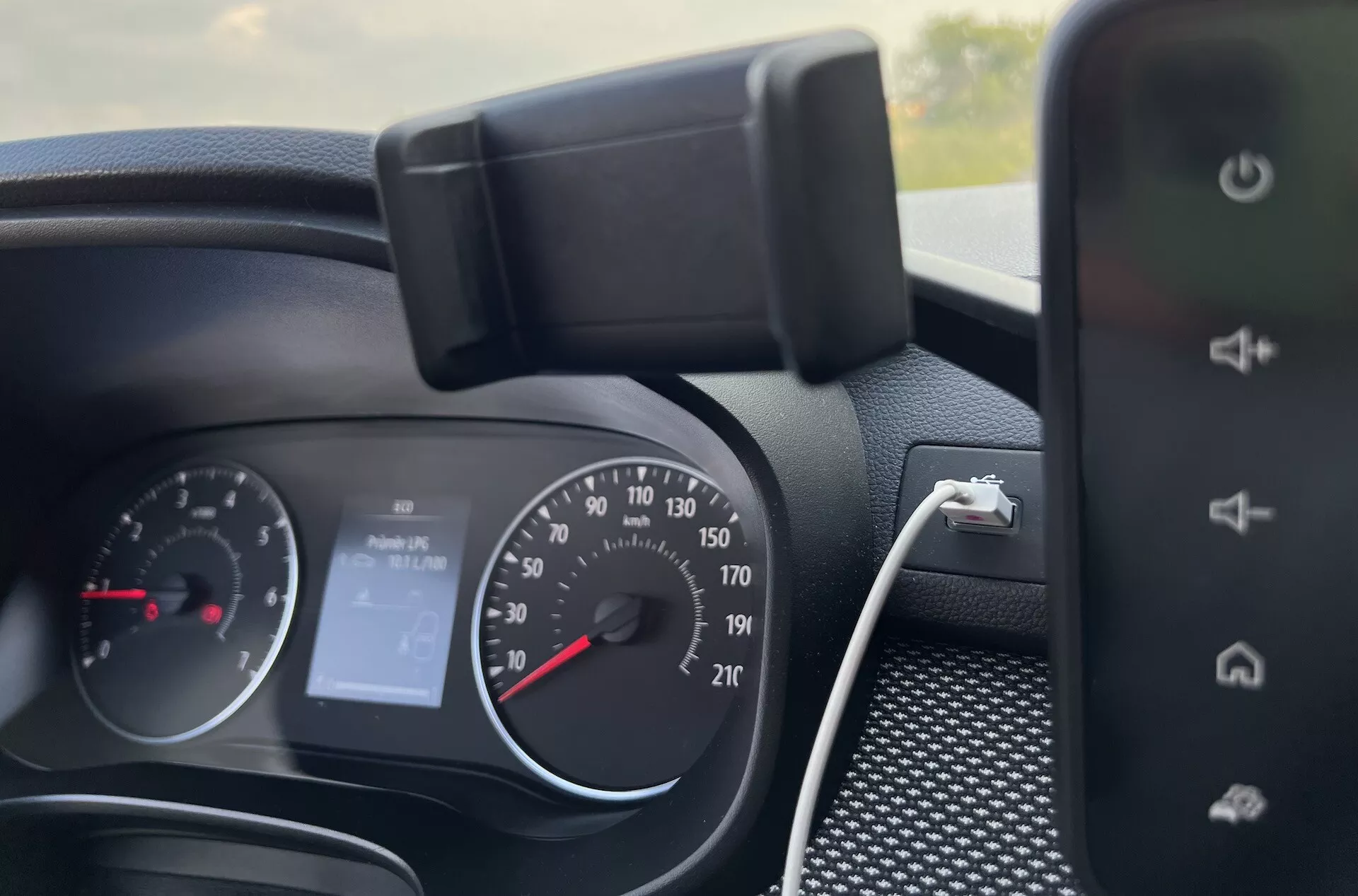 Vue intérieure détaillée du tableau de bord de la Dacia Jogger 2022 montrant le cluster d'instrumentation, les commandes au volant et une partie du système d'infodivertissement, indiquant des fonctionnalités comme un compteur de vitesse de style analogique, un tachymètre, un affichage numérique pour 'Pas d'Audio' et des capacités de chargement de smartphone.