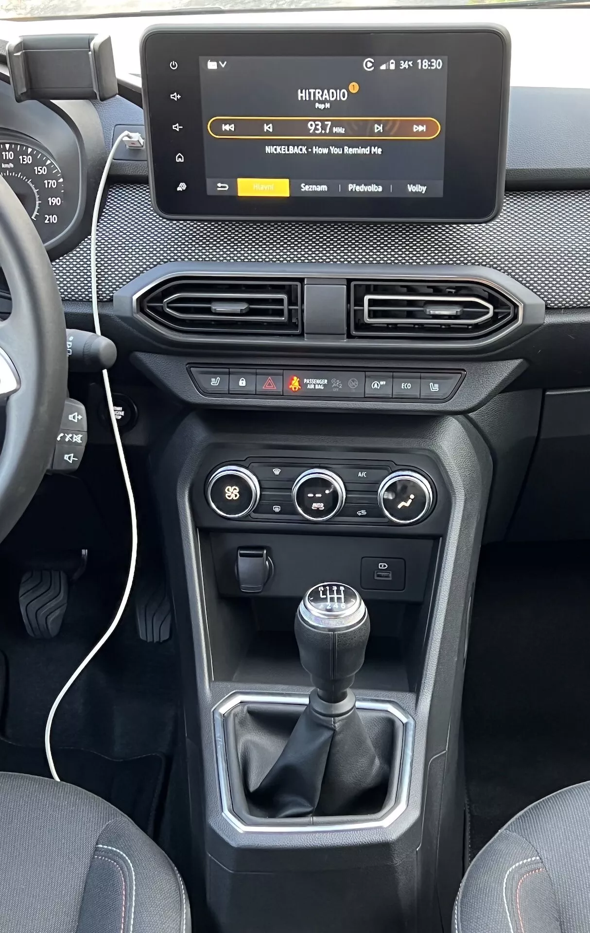 Vue intérieure de la Dacia Jogger 2022 centrée sur la console centrale et le tableau de bord, affichant un écran tactile flottant pour l'infodivertissement, des aérations, des commandes de climatisation et véhicule, et un levier de vitesse manuel