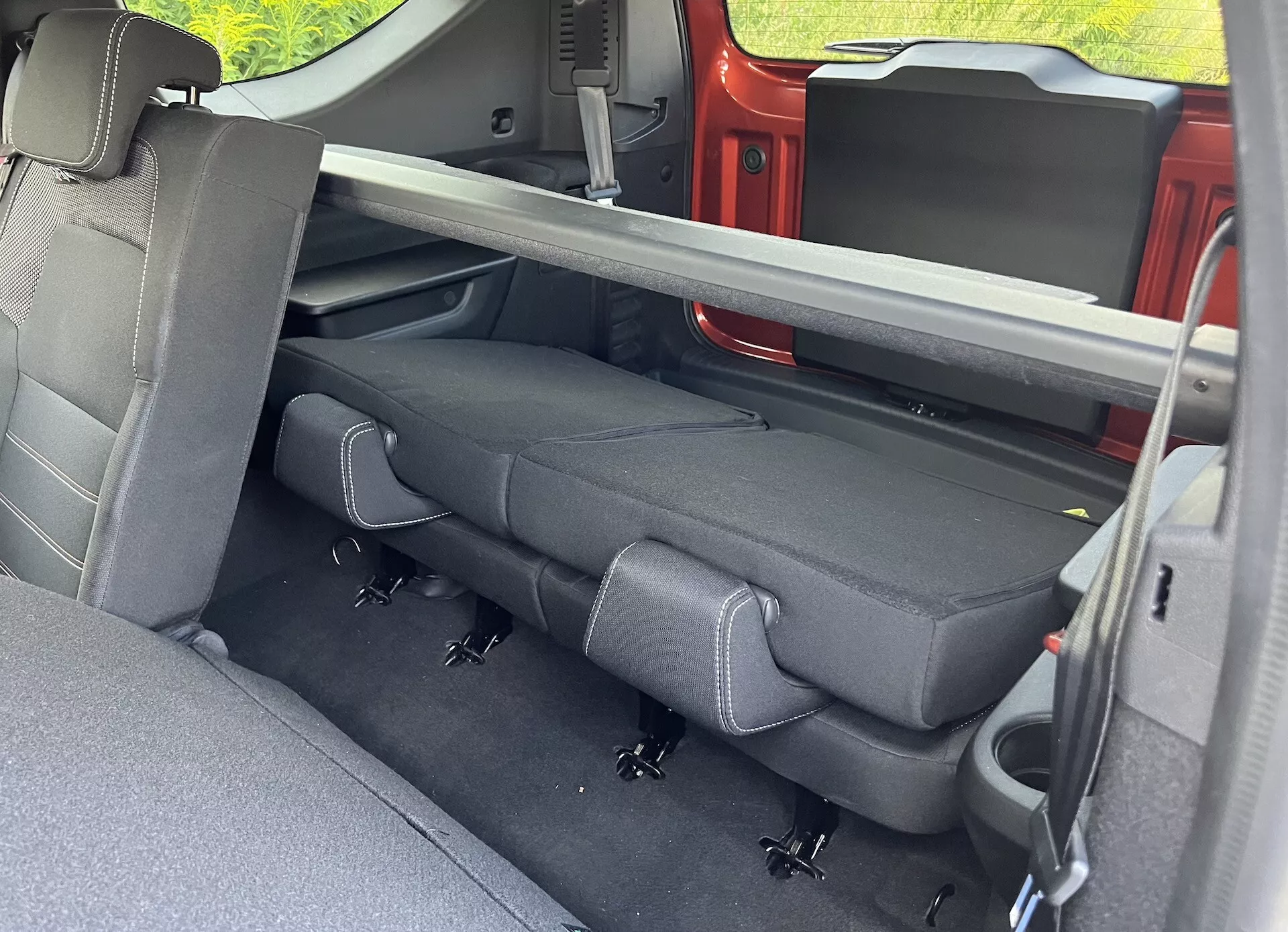 Vue intérieure du Dacia Jogger 2022 centrée sur le compartiment passagers arrière avec une sellerie foncée, des ceintures de sécurité rétractables, le système LATCH et un mécanisme de sièges pliables, vue depuis la porte arrière côté passager.