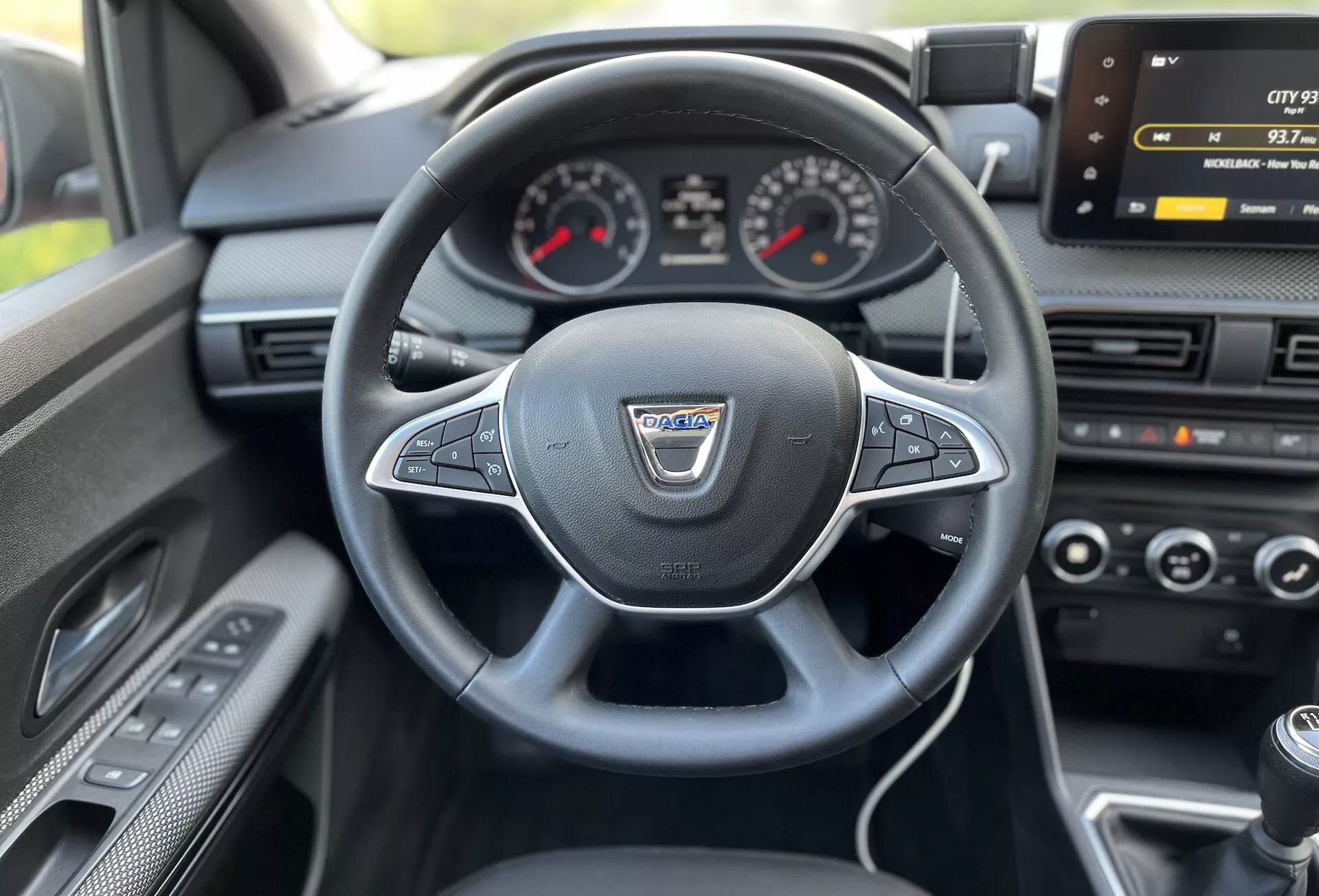 Vue intérieure d'une Dacia Jogger 2022 depuis le siège du conducteur montrant le volant multifonction enveloppé de cuir, tableau de bord analogique avec affichage numérique central, écran d'infodivertissement, contrôle climatique et levier de vitesse manuel