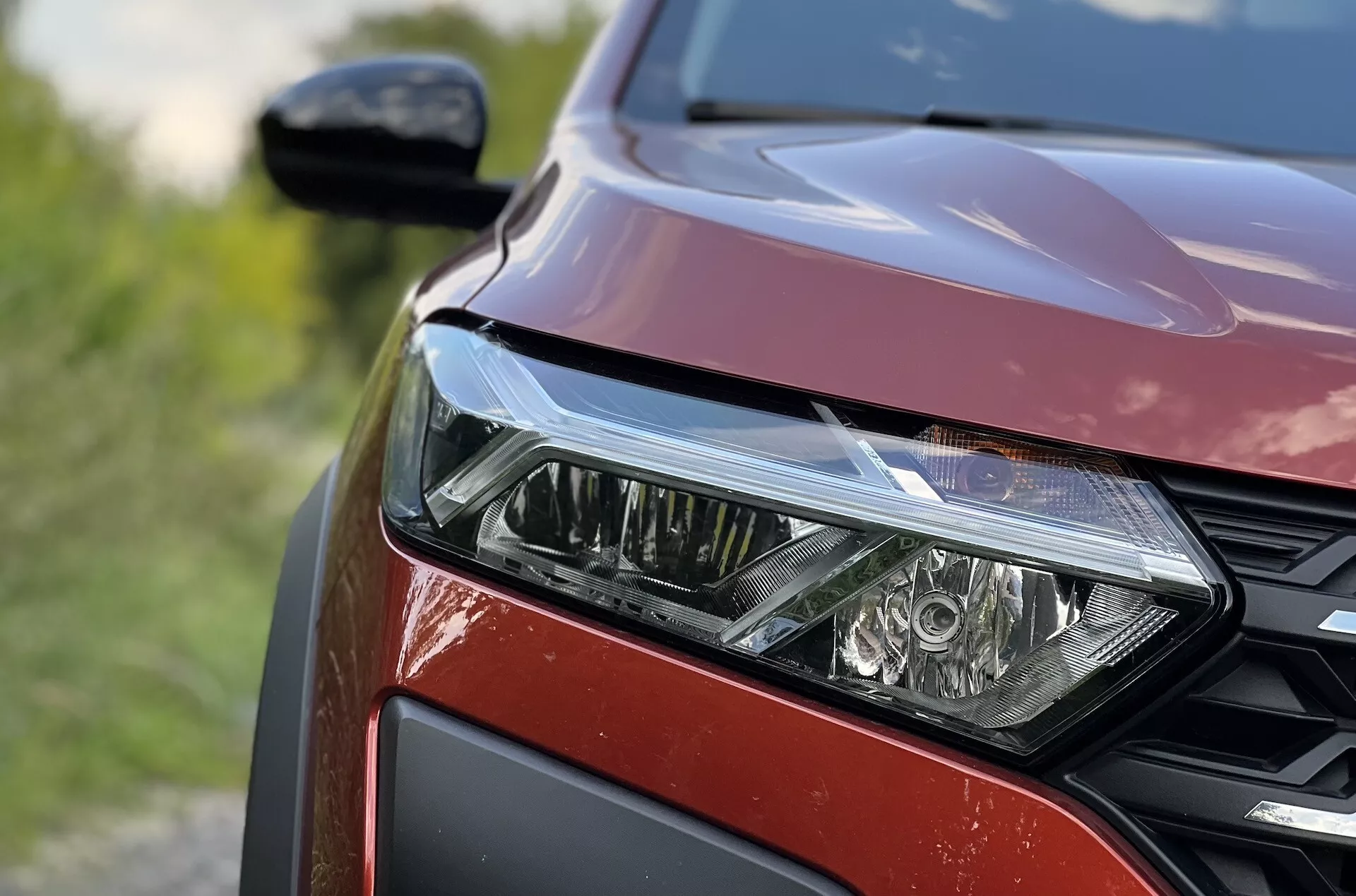 Vue rapprochée du côté avant gauche de la Dacia Jogger 2022 mettant en évidence l'ensemble phare LED, le motif de grille en nid d'abeille et la finition de peinture rouge métallisé