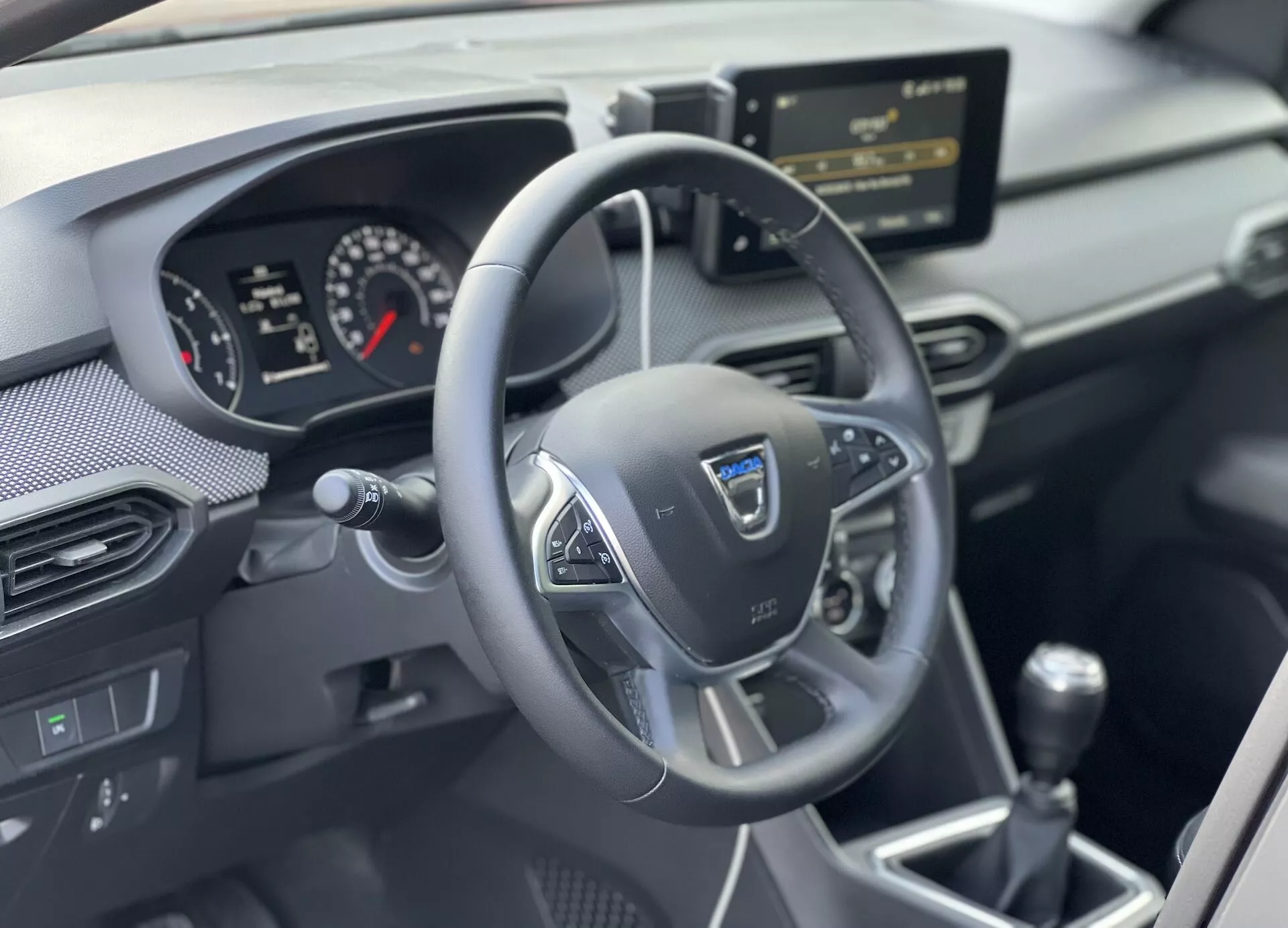 Vue intérieure du Dacia Jogger 2022 se concentrant sur la zone du conducteur avec un volant multifonction à trois branches, un tableau de bord analogique-numérique, la console centrale avec un système d'infodivertissement et un levier de vitesses manuel