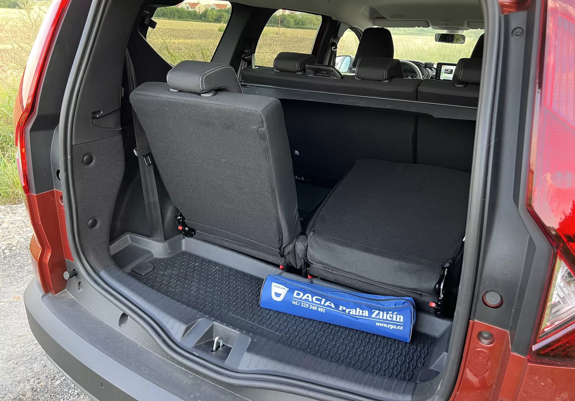 Dacia Jogger 2022 montrant l'espace de chargement intérieur depuis un angle latéral gauche avec le coffre ouvert, présentant une zone de chargement plate avec un tapis en caoutchouc, des sièges arrière rabattables 60/40 et des détails de garniture latérale sans composants technologiques avancés ou de luxe visibles