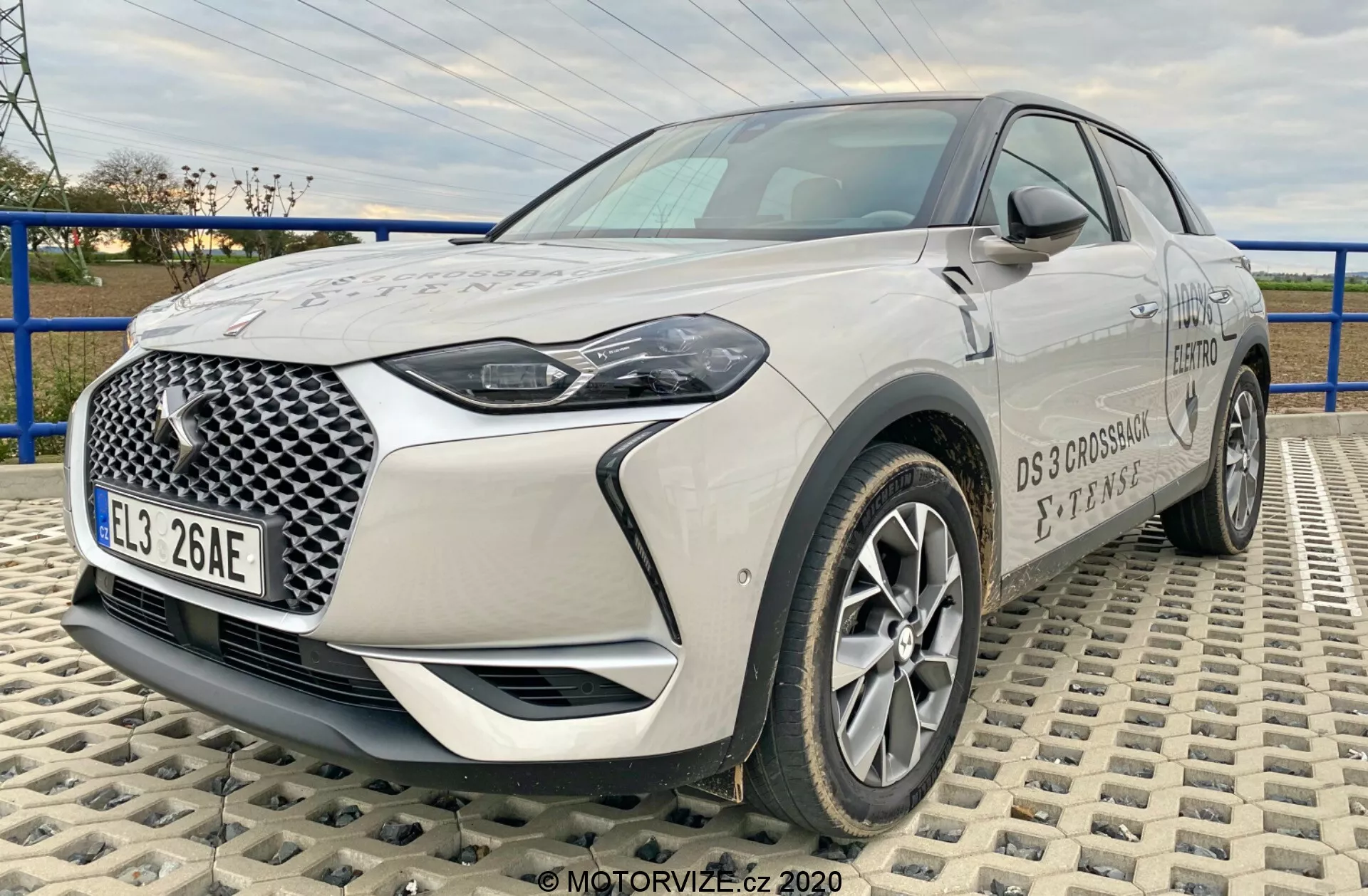 L'image montre le SUV crossover moderne DS-Automobiles DS-3 2019 (DS-3 Crossback E-Tense), capturé à un angle de trois quarts avant sur une surface texturée faite de carreaux imbriqués. La perspective de hauteur faible à moyenne met en valeur la stature de la voiture, offrant une vue complète de sa calandre avant avec un motif géométrique distinctif, phares à LED, jantes en alliage, rétroviseurs et détails de la marque. La longueur et les caractéristiques de conception frontale du véhicule sont clairement visibles, mettant en évidence sa technologie automobile moderne et avancée.