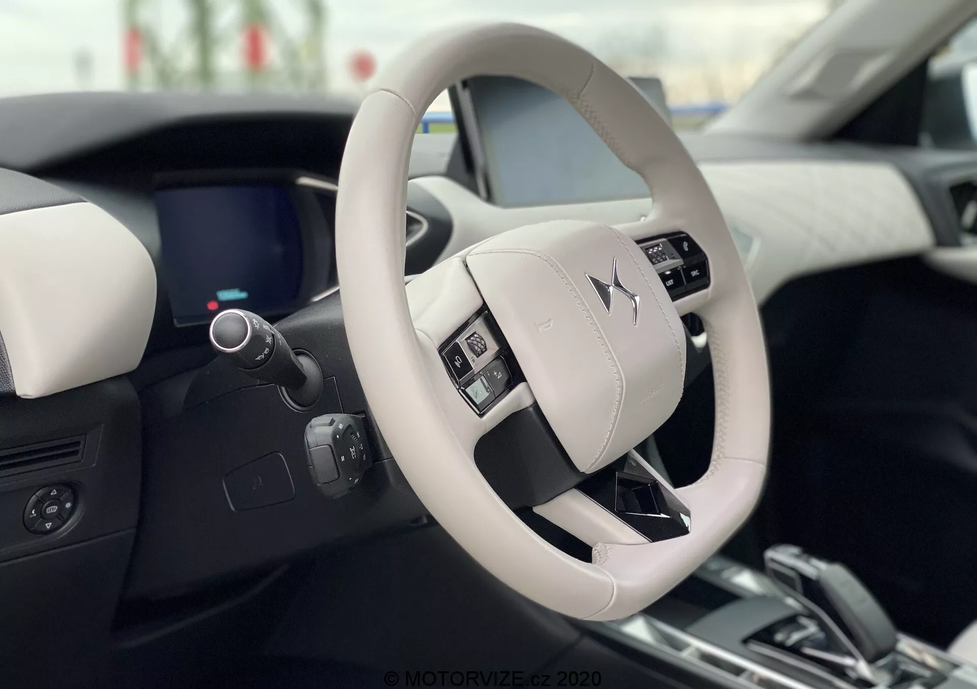 Vue intérieure de la DS Automobiles DS 3 Crossback E-Tense 2019, montrant le design moderne et luxueux du volant et du tableau de bord depuis la perspective du siège du conducteur. Le volant de couleur claire comporte des boutons de commande et affiche en évidence le logo du fabricant. Le tableau de bord numérique élégant, partiellement visible derrière le volant, complète le design intérieur bicolore avec des matériaux de haute qualité.