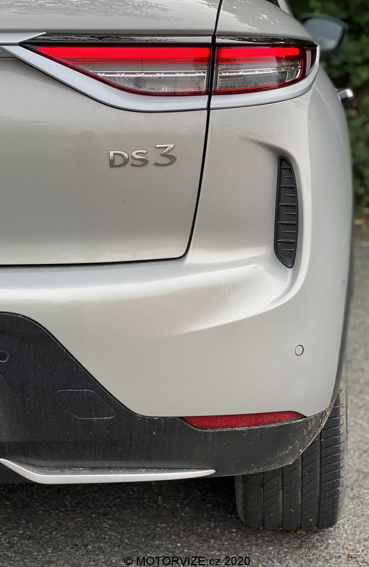 Vue rapprochée de l'arrière latéral d'une DS Automobiles DS 3 Crossback E-Tense 2019, se concentrant sur la partie supérieure droite du pare-chocs arrière, le coffre et une partie de l'aile arrière droite. L'image capture les détails distinctifs du design du modèle, notamment les feux arrière à LED fins, le badge 'DS 3' en relief, les capteurs de stationnement et l'élément en plastique noir sur le pare-chocs. La voiture, présentée dans une teinte claire avec une finition métallique, est photographiée à la lumière naturelle, mettant en valeur les détails fins de la peinture et de la texture.