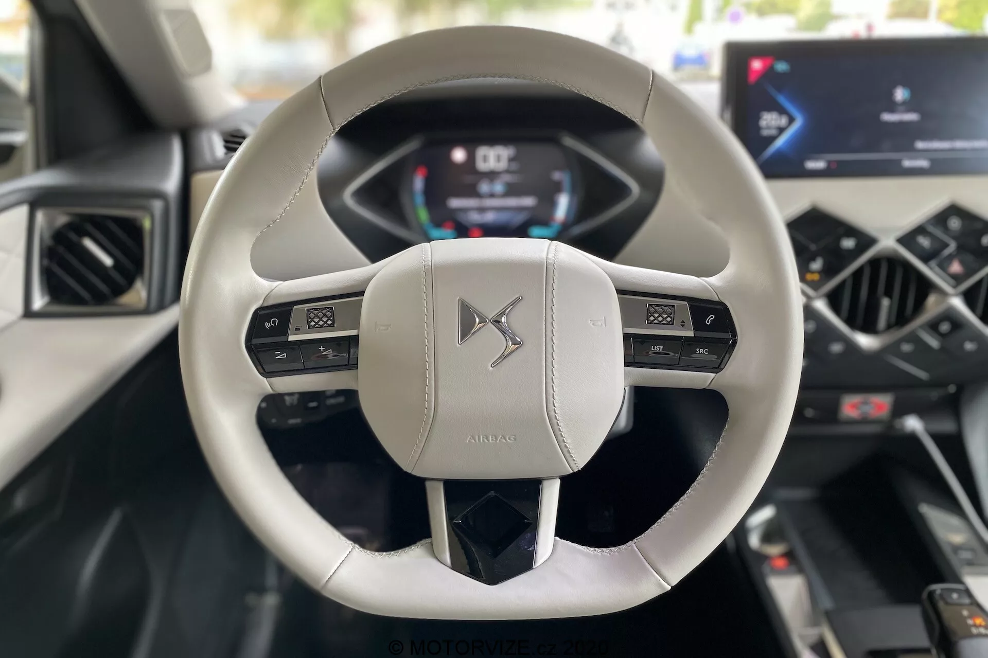Vue intérieure depuis la perspective du conducteur dans une DS Automobiles DS 3 Crossback E-Tense 2019, avec mise en avant du volant moderne à deux branches, recouvert de cuir clair, avec des commandes multifonctions et un tableau de bord numérique affichant la vitesse et les tours par minute. La console centrale dispose d'un écran tactile d'infodivertissement intégré et de commandes minimalistes pour la climatisation, mettant en valeur une technologie automobile avancée et un design luxueux.