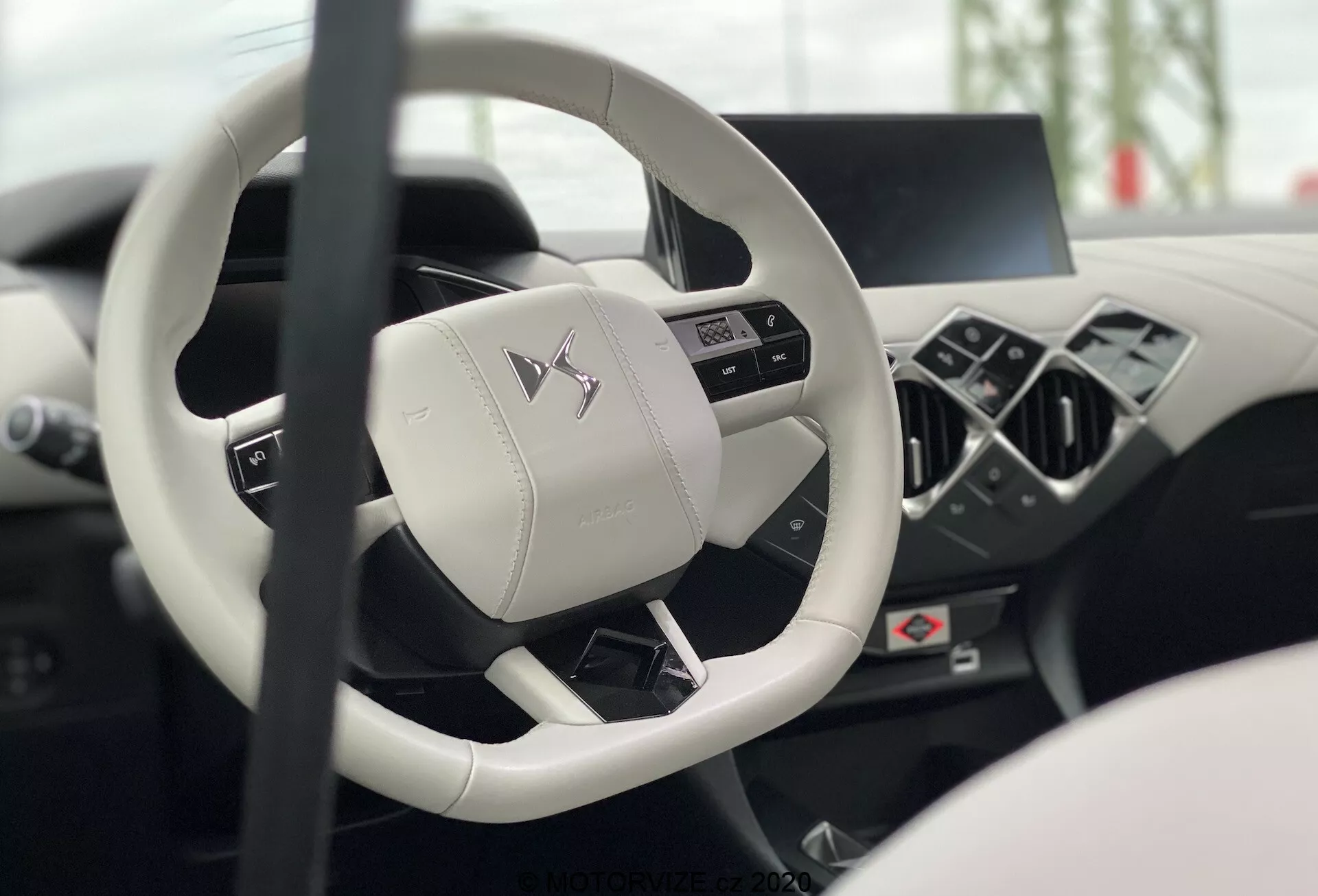 Intérieur de la DS Automobiles DS-3 2019 (DS-3-Crossback-E-Tense) depuis le siège du conducteur, se concentrant sur le volant moderne à fond plat et trois branches avec des boutons multifonctionnels et un tableau de bord numérique flou et une console centrale montrant le luxe et la technologie avancée