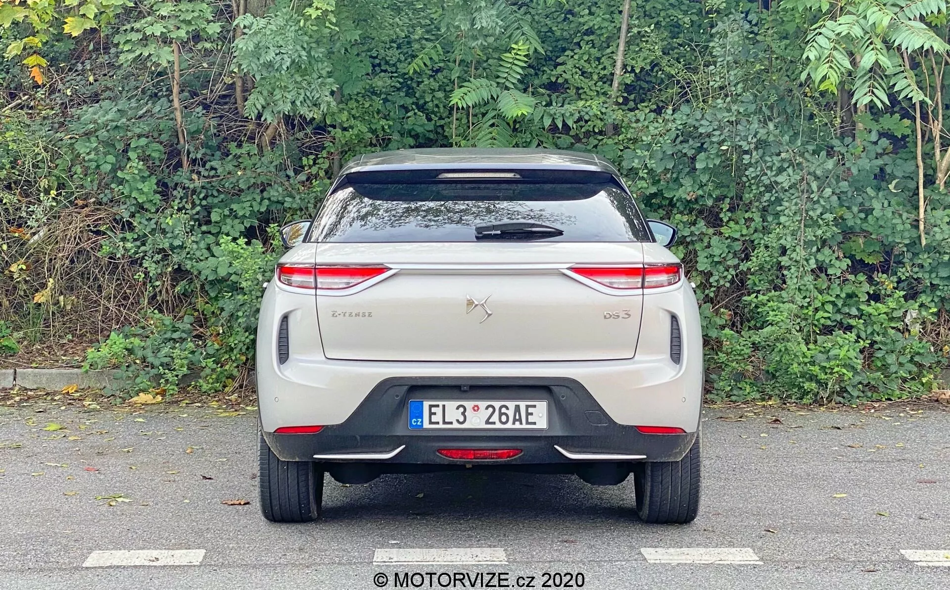 L'image montre une vue arrière de la DS Automobiles DS 3 Crossback E-Tense 2019, photographiée au niveau des yeux en se concentrant sur l'arrière. Les éléments visibles incluent une plaque d'immatriculation centrée, des badges de marque et de modèle sur le coffre, des feux arrière modernes orientés horizontalement avec des motifs lumineux LED complexes, un pare-brise arrière avec essuie-glace, un spoiler de toit, et un pare-chocs avec une bande réfléchissante. Aucun tuyau d'échappement traditionnel n'est visible, ce qui suggère qu'il s'agit d'un véhicule électrique. Le design est épuré, probablement en incorporant des caractéristiques technologiques avancées typiques des voitures électriques ou hybrides.