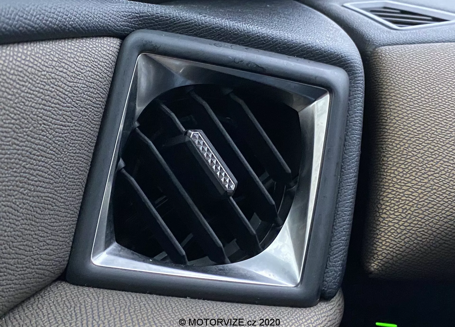 Vue rapprochée de la bouche d'aération de l'intérieur du véhicule DS Automobiles DS-3 Crossback 2019, présentant des lamelles horizontales réglables dans une ouverture en forme de diamant, entourée d'une surface de tableau de bord en plastique texturé avec un encadrement carré pour un design supplémentaire.
