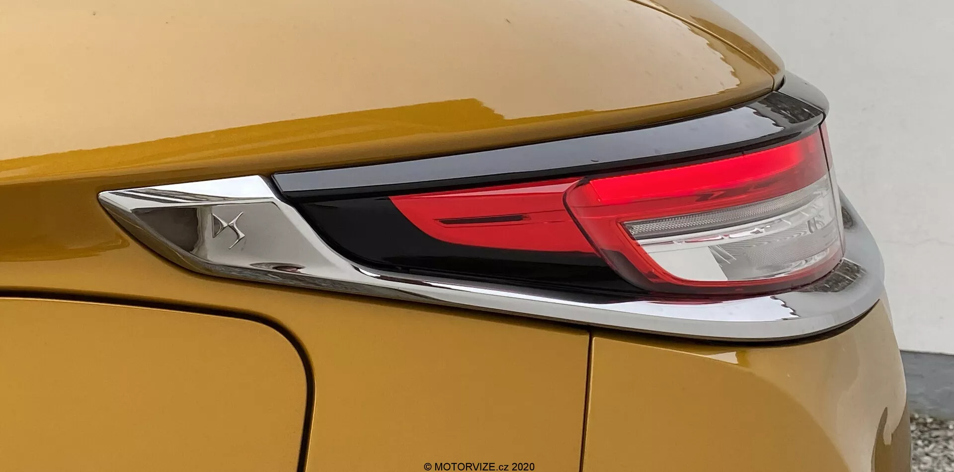 Vue rapprochée de la section arrière de la DS Automobiles DS-3 2019 (DS-3 Crossback). L'image se concentre sur le côté droit du véhicule, mettant en évidence une carrosserie de couleur or ou bronze métallique, une partie de l'ensemble des feux arrière à LED, et un panneau arrière lisse et incurvé avec une ligne de caractère prononcée. Un emblème chromé est également visible, mais il ne révèle pas la marque.