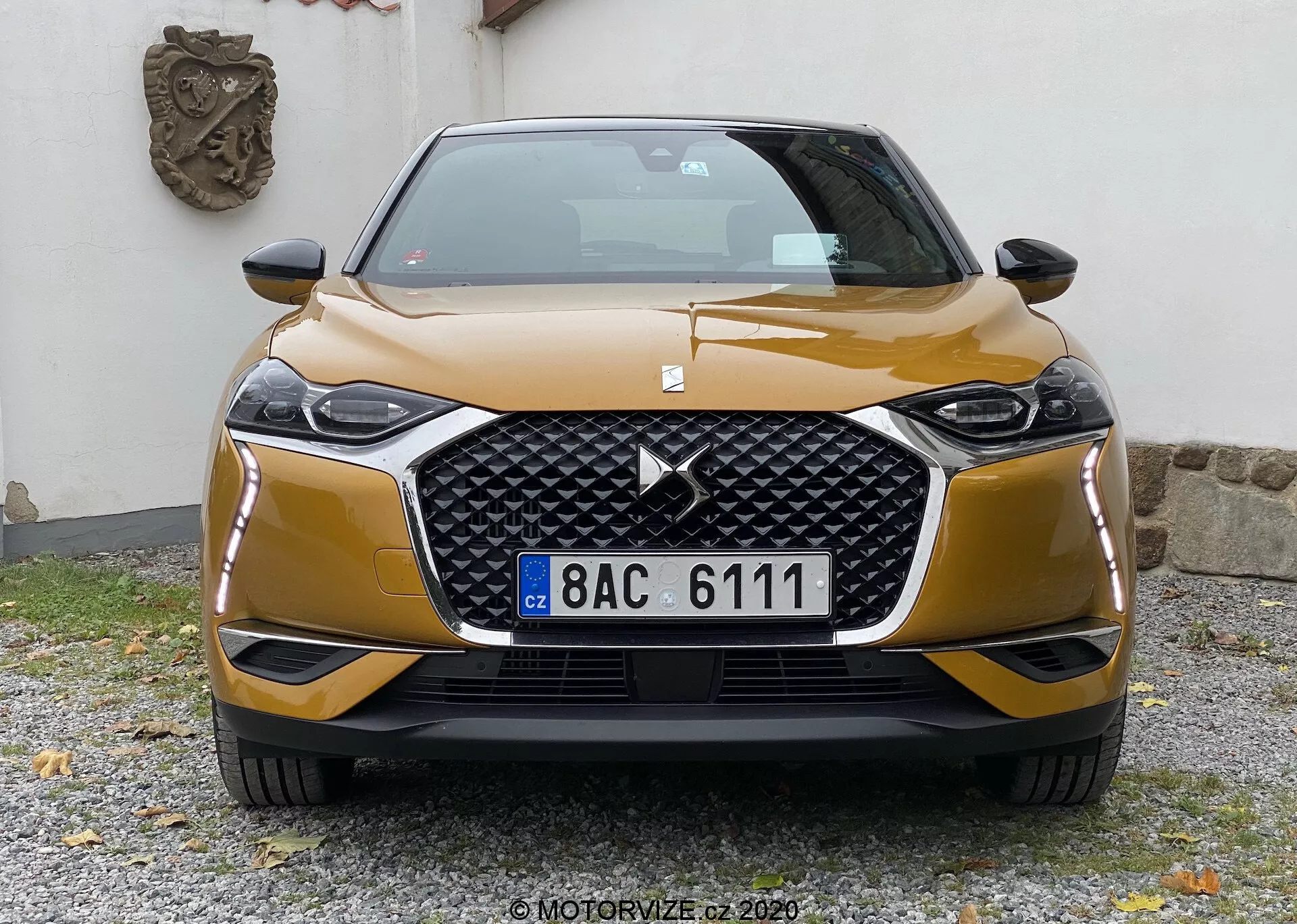 Vue de face de la DS-3 Crossback 2019, mettant en avant sa grille hexagonale proéminente avec un grand logo centré et flanquée de blocs de phares angulaires élégants avec technologie LED ou HID probable. Le pare-chocs avant sportif avec une garniture contrastante et les lignes sculptées du capot ajoutent une dynamique esthétique. La voiture légèrement décalée vers la droite est photographiée à hauteur de calandre, capturant un design et une technologie modernes.