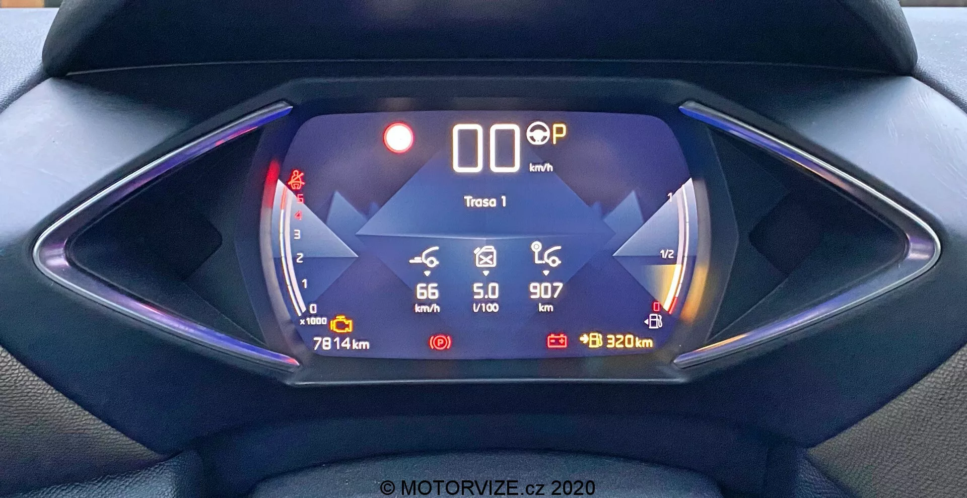 Tableau de bord numérique du DS Automobiles DS-3 2019 (DS-3 Crossback) vu de la perspective du conducteur. Composition symétrique se concentrant sur le tableau de bord hexagonal futuriste avec un affichage numérique dominé par le bleu. Les fonctions incluent un indicateur d'autonomie de la batterie affichant '66 km' à gauche, une vitesse de '0 km/h' au centre, la position de la vitesse 'P', un icône de route glissante et un indicateur de '320 m' à droite. Les données supplémentaires incluent la température extérieure '5,0°C', l'heure actuelle '9:07' et le kilométrage du véhicule '7814 km'. Cette image met en évidence les caractéristiques d'un véhicule électrique ou hybride avec des technologies avancées et des infographies numériques.