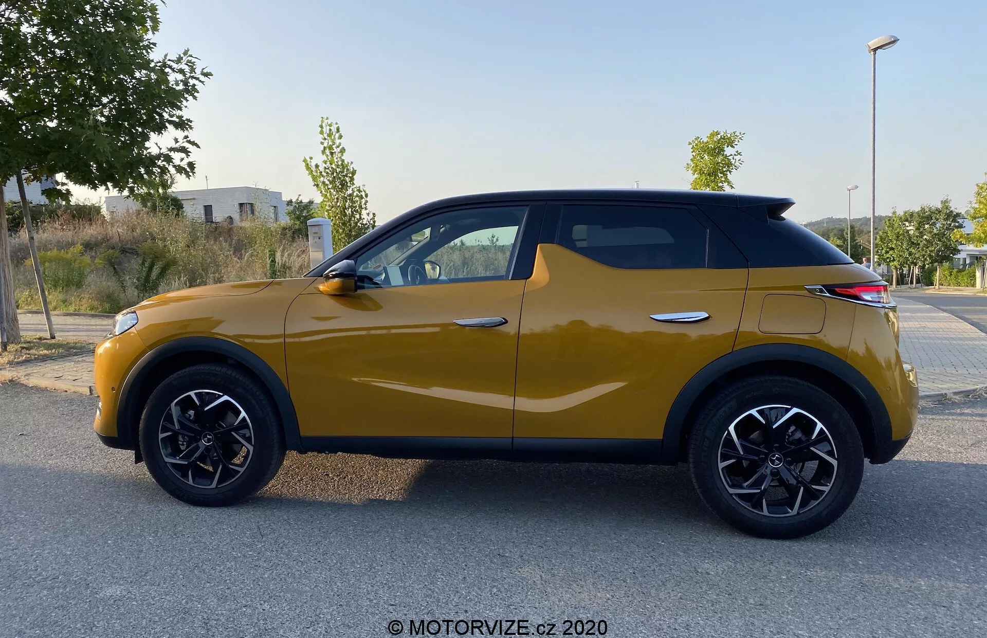 Vue de profil latéral du DS Automobiles DS 3 Crossback 2019 de couleur jaune moutarde. Le SUV compact moderne présente des arches de roue noires distinctives, des jantes en alliage multibranches noires et une ligne dynamique de carrosserie allant de l'arche de roue avant aux feux arrière. Les rétroviseurs latéraux intègrent des clignotants et les fenêtres sont entourées de contours noirs, soulignant un design cohérent, tandis qu'une silhouette de type coupé ajoute une touche contemporaine. L'image, prise sous un éclairage diffus, ne présente ni ombres ni éblouissements, permettant de se concentrer sur les éléments de conception du véhicule.