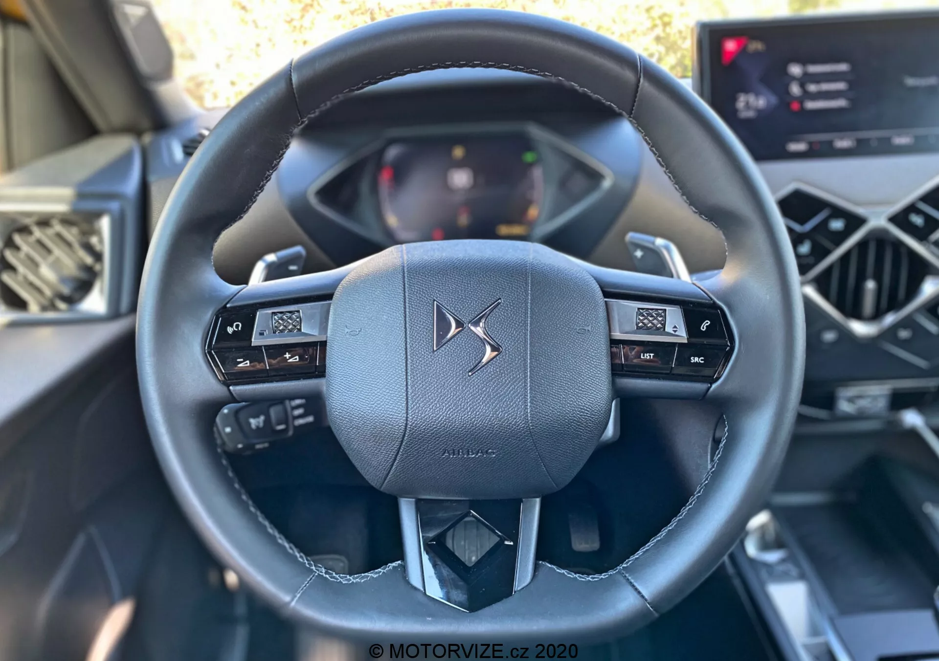 Photo de l'intérieur de la DS Automobiles DS-3 Crossback 2019 centrée sur le volant luxueux en cuir vue du siège conducteur. Le volant multifonctionnel comporte des boutons de contrôle pour l'audio et l'affichage des informations du véhicule. Un tableau de bord numérique et un système d'infodivertissement à écran tactile moderne sont également partiellement visibles, mettant en valeur les interfaces électroniques avancées de cet intérieur de voiture contemporain.