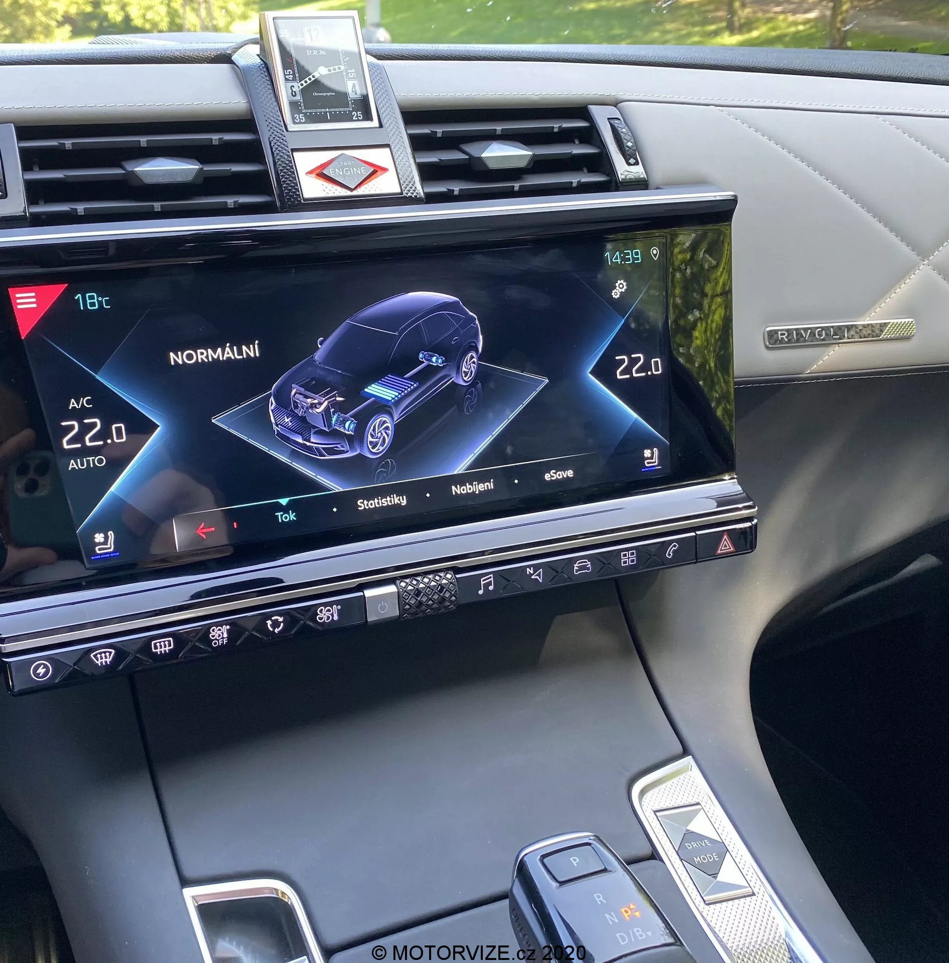 Console centrale de la DS Automobiles DS-7 Crossback 2018, affichant l'écran du système d'infodivertissement avec une représentation graphique 3D de la voiture depuis une perspective avant droite, indiquant son état et divers réglages tels que la climatisation, le chauffage des sièges et les fonctionnalités interactives du modèle de voiture, ainsi que des boutons physiques, des commandes tactiles et une vue partielle du levier de vitesses et du sélecteur de mode de conduite.