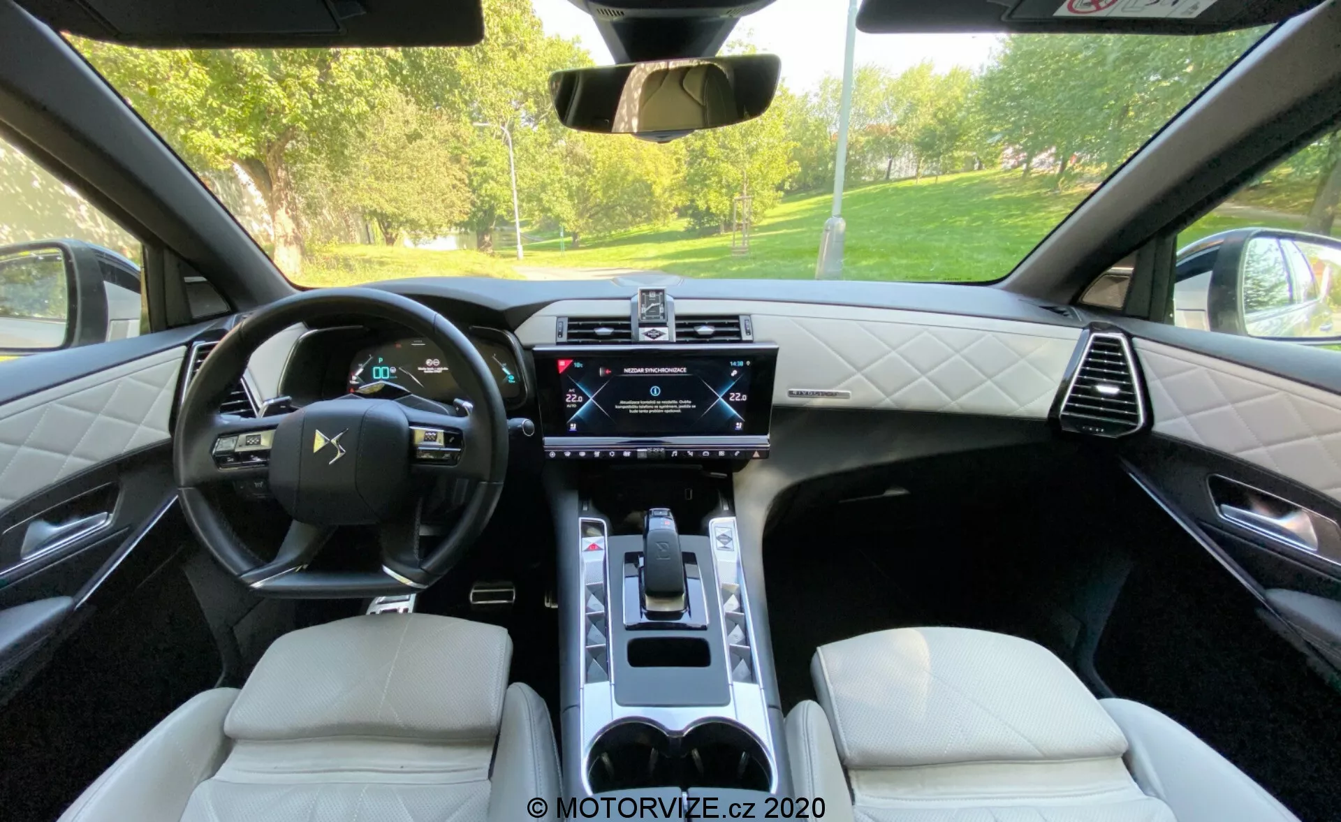 Vue intérieure de la DS Automobiles DS 7 Crossback 2018 depuis la banquette arrière, mettant en valeur le volant multifonction en cuir, le tableau de bord numérique, l'écran tactile central d'infodivertissement, le panneau de commande du climat, le sélecteur de vitesse électronique, les sièges en cuir avec coutures en losange et la console centrale avec porte-gobelets. L'image montre une combinaison de technologie de pointe et de design sophistiqué.