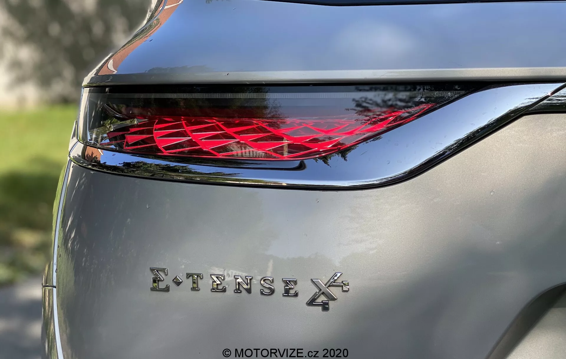 Gros plan de la section arrière du DS Automobiles DS-7 2018 (DS-7 Crossback) montrant un feu arrière LED complexe avec une courbure horizontale et un badge chromé 'EXTENSE 4X', mettant en avant l'éclairage automobile high-tech et la transmission intégrale. Prise en lumière naturelle avec carrosserie argentée.