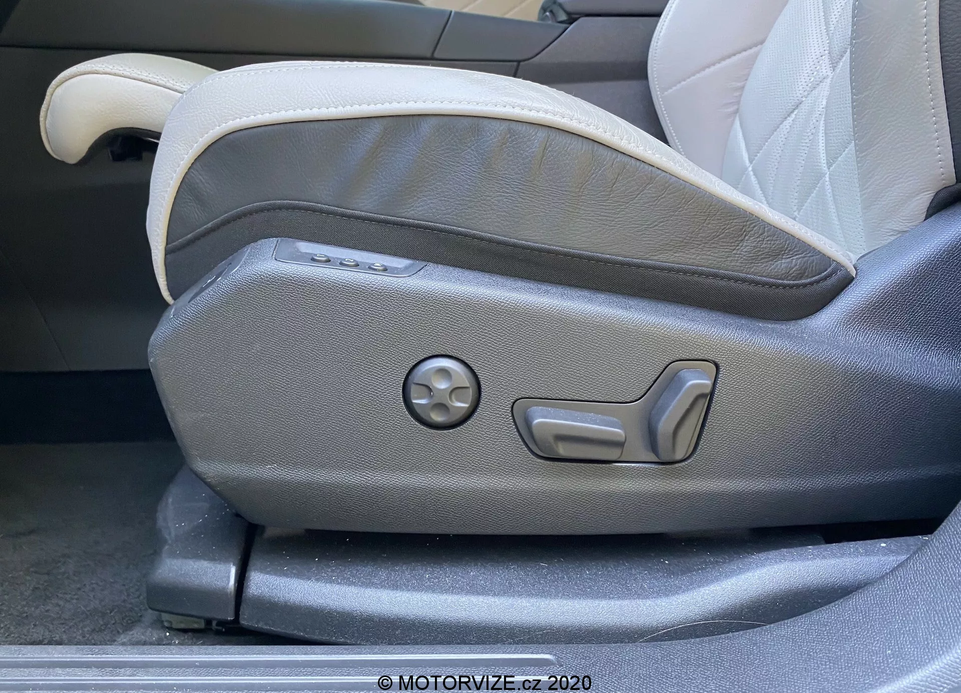 Gros plan sur le panneau de réglage du siège avant côté conducteur d'une DS Automobiles DS 7 Crossback 2018. L'image capture les commandes de réglage du siège électrifiées, y compris les boutons pour le réglage multi-niveaux et un cadran rond pour les réglages de mémoire. Le siège présente une sellerie bicolore en gris clair et foncé, affichant un design moderne et ergonomique caractéristique des intérieurs de voitures de luxe.