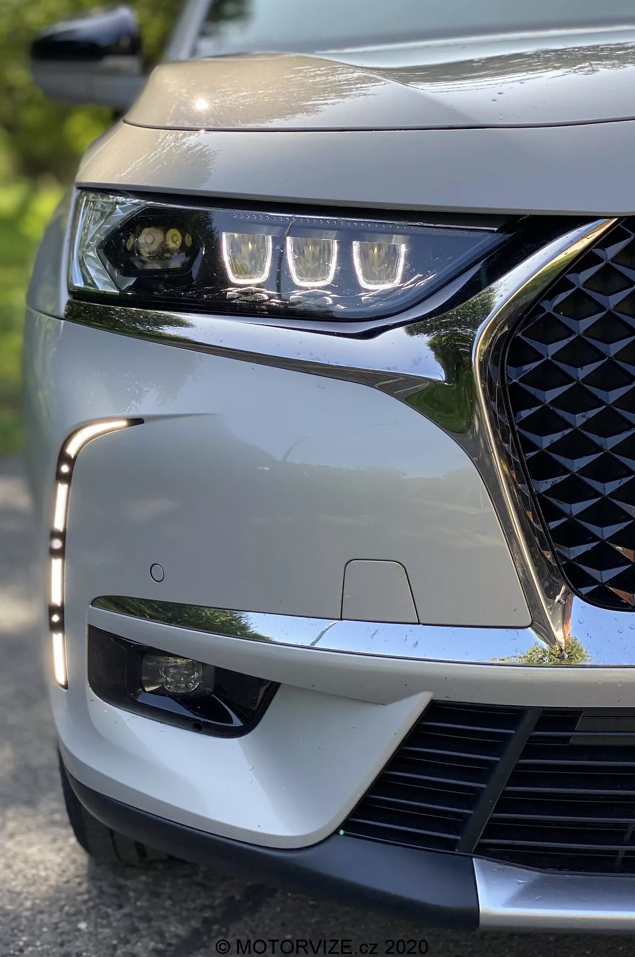 Gros plan en contre-plongée du DS Automobiles DS 7 Crossback 2018, focalisé sur le quart avant gauche. Points forts : les phares LED élégants, la calandre à motif géométrique, le pare-chocs avant sportif et le capteur ADAS visible, mettant en valeur les caractéristiques technologiques et esthétiques modernes du véhicule.