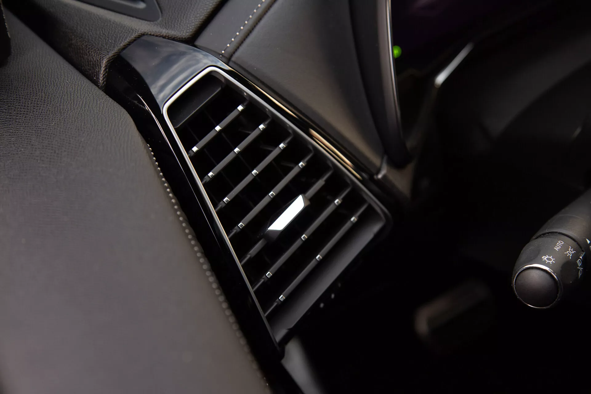 Vue rapprochée de la bouche d'air de la DS Automobiles DS-7 2022 sur le tableau de bord avec des lamelles noires réglables alignées verticalement, une lunette brillante et un accent argenté sur la commande, démontrant la qualité du design intérieur et des matériaux du véhicule