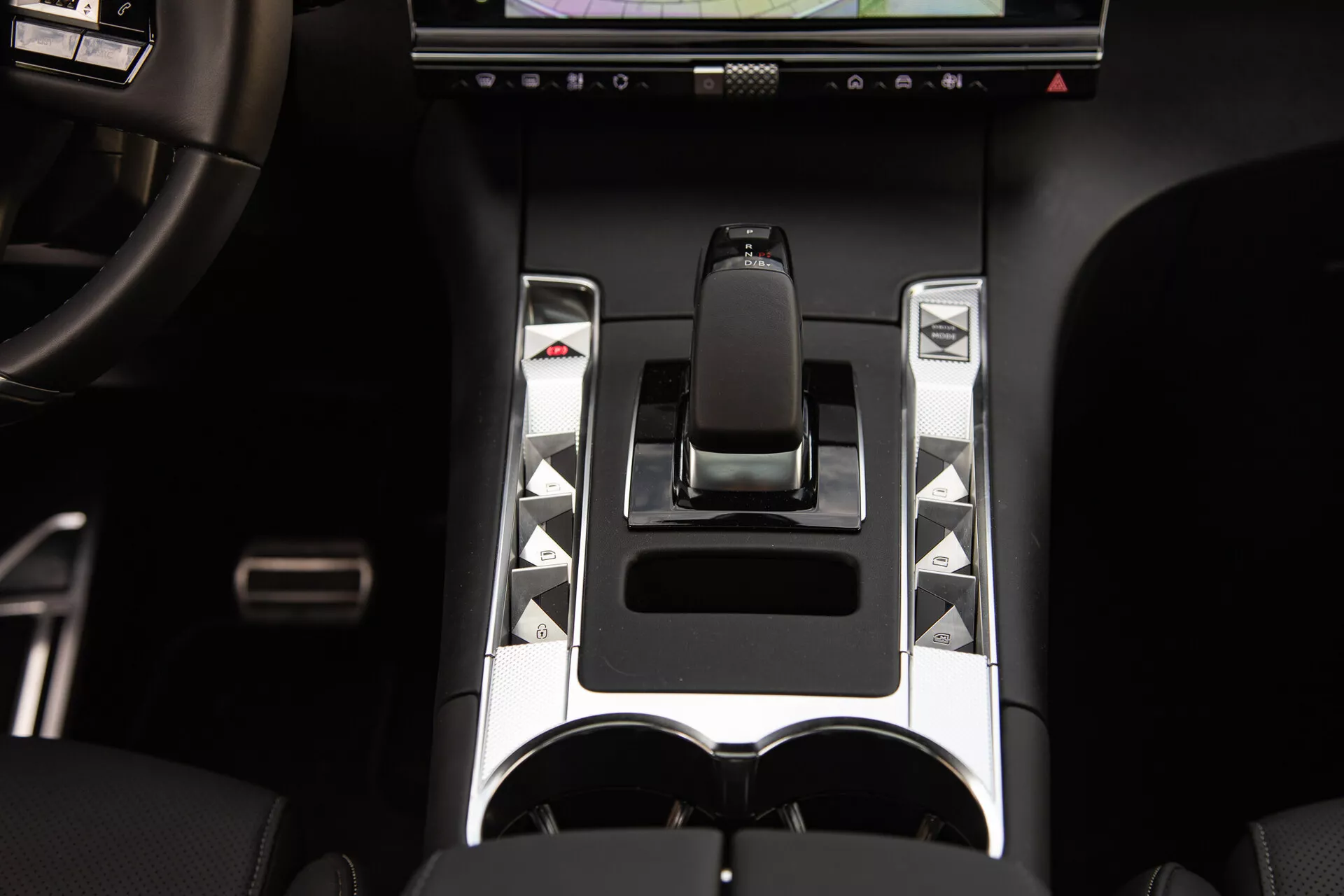 Vue détaillée de la console centrale du DS Automobiles DS-7 2022 présentant un levier de vitesse ergonomique, des accents métalliques, des boutons de commande uniques, un écran tactile et des porte-gobelets doubles, mettant en évidence des éléments de contrôle avancés du véhicule et de design de luxe.