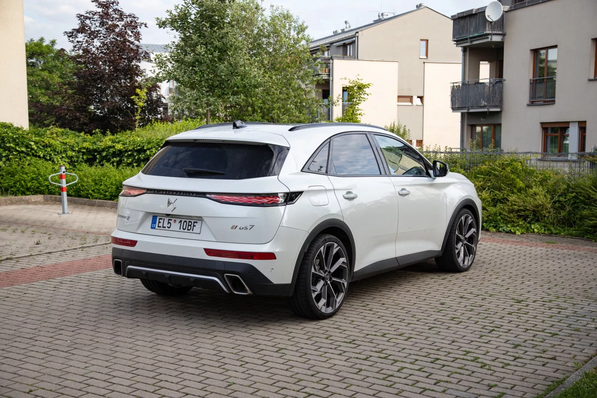 SUV blanc DS Automobiles DS-7 de 2022 stationné sur une zone pavée de briques, présentant des feux arrière LED, un système d'échappement double et des roues en alliage sport. L'image saisit le design élégant de type SUV coupé du véhicule depuis une perspective arrière aux trois quarts, mettant en lumière un possible toit panoramique et des rétroviseurs latéraux à la pointe de la technologie.