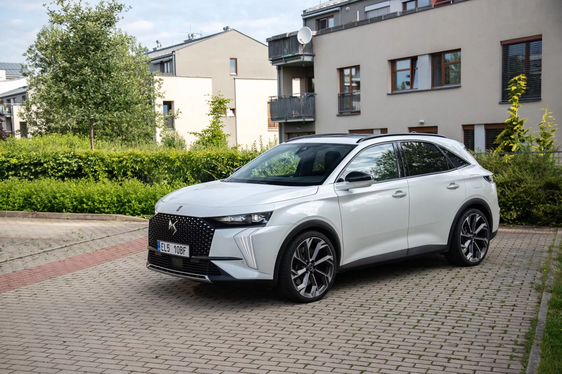 Vue avant trois-quarts du crossover DS Automobiles DS-7 2022 garé sur une rue résidentielle pavée de briques, présentant son design moderne incluant une grille avant distinctive, des phares LED élégants, un capot sculpté, de grandes roues en alliage et un profil latéral sportif avec des clignotants intégrés sur les rétroviseurs latéraux montés sur la porte sous la lumière naturelle du jour.