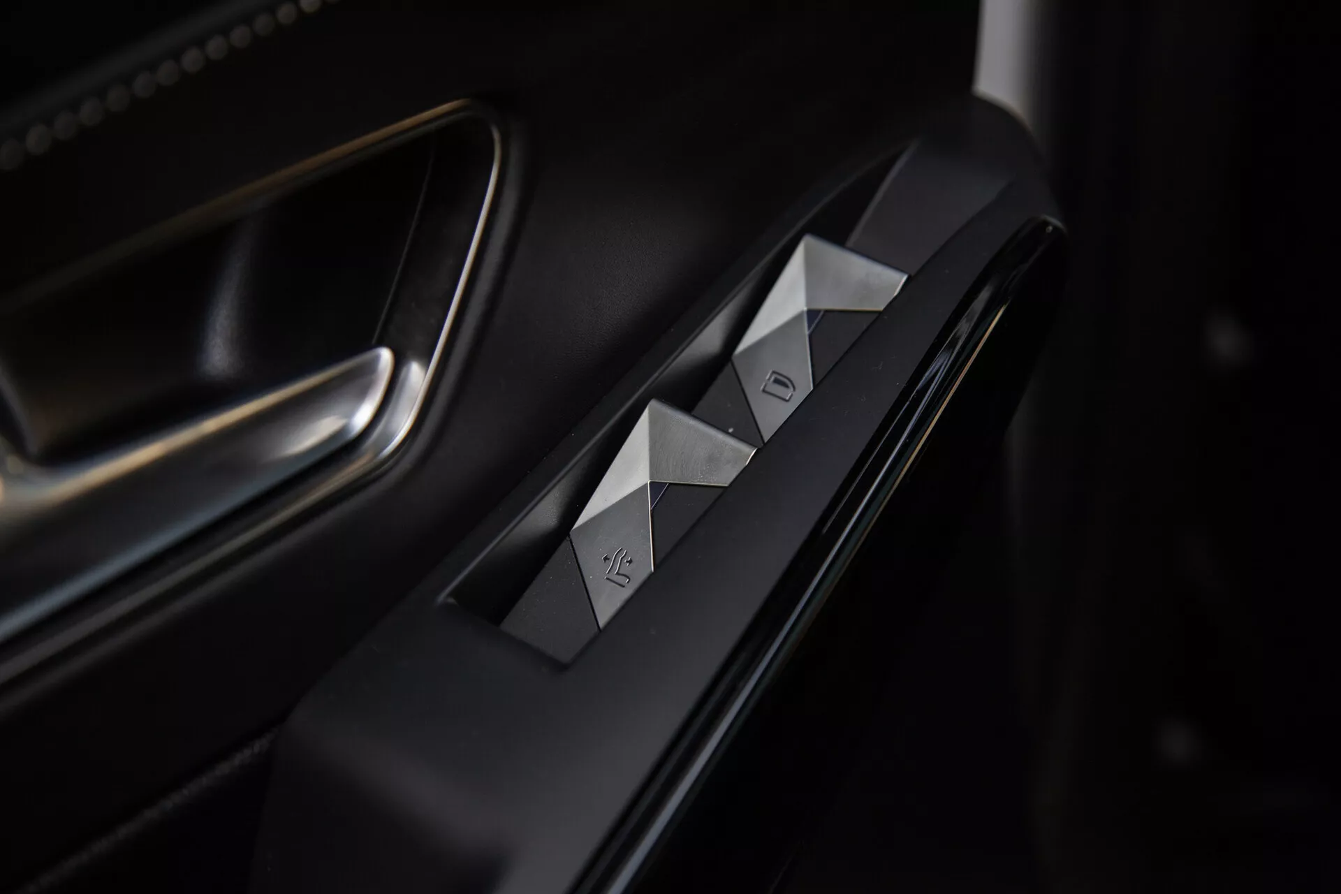 Vue détaillée des commandes de porte côté conducteur de la DS Automobiles DS-7 2022, avec des interrupteurs de fenêtre à coupe diamant, bouton de verrouillage de porte, finitions haut de gamme en mat et métallique, et éclairage sophistiqué soulignant la conception ergonomique.