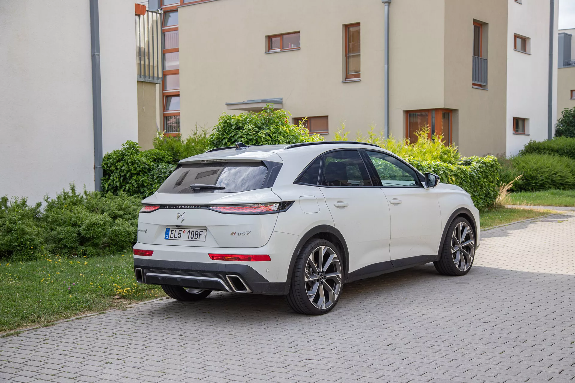 DS Automobiles DS-7 2022 garée sur une allée à côté d'une zone herbeuse, mettant en évidence sa vue arrière trois quarts avec feux arrière LED, diffuseur arrière, double échappement, spoiler de toit, antenne aileron de requin et jantes alliage à cinq branches.