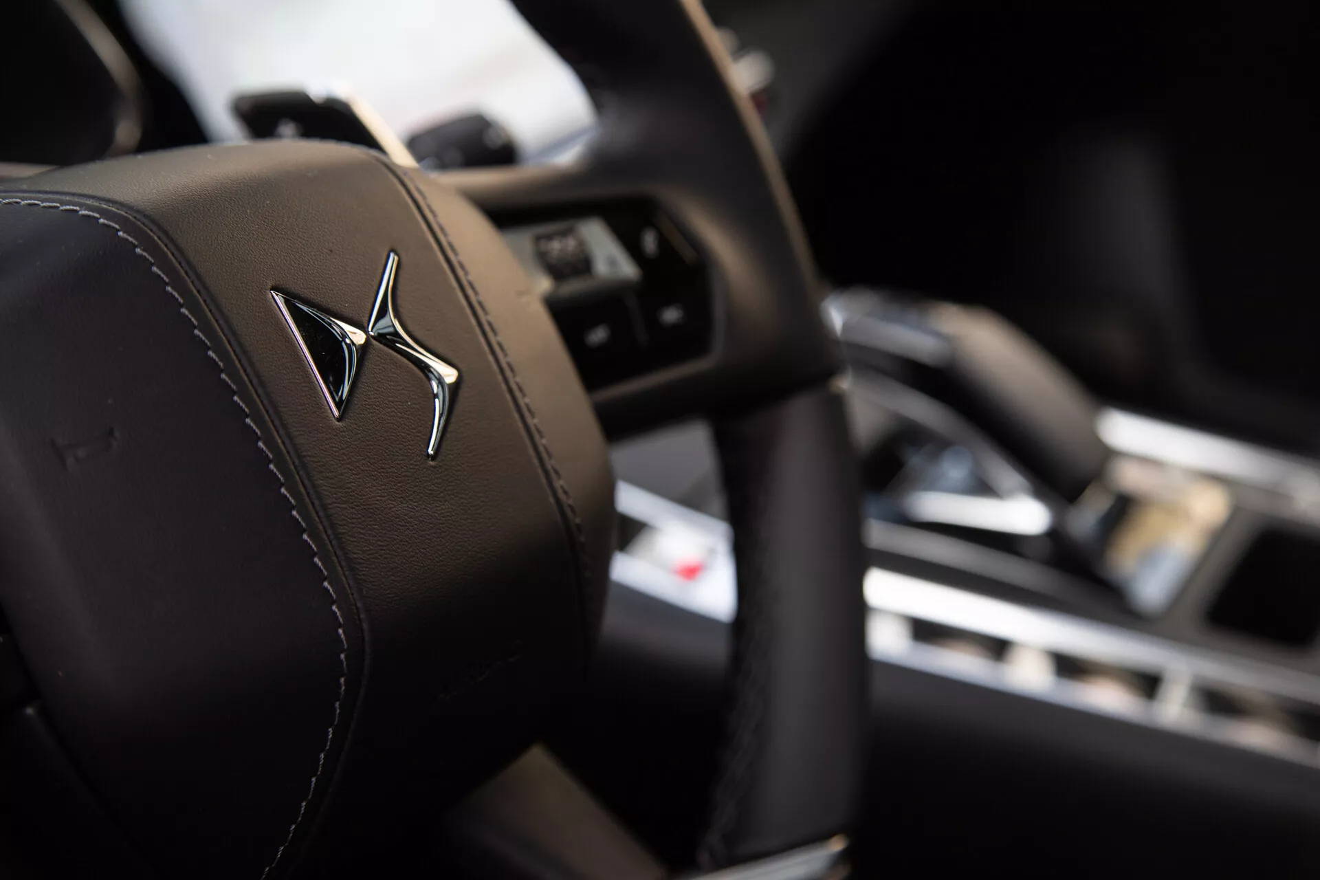 Vue rapprochée de l'appui-tête du siège conducteur avec un logo en relief, avec une faible profondeur de champ mettant en évidence l'appui-tête au point net contre un arrière-plan intérieur flou montrant un volant avec des boutons de contrôle et un tableau de bord avec écran central.