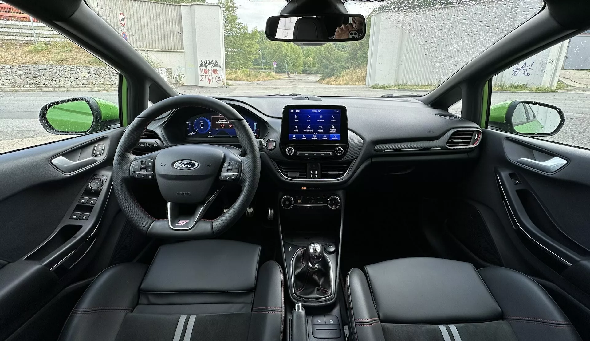 Vue intérieure de la Ford Fiesta 2022 depuis le siège arrière, montrant l'ensemble du cockpit avec tableau de bord numérique, volant multifonctions et sièges en cuir avec accents de couture