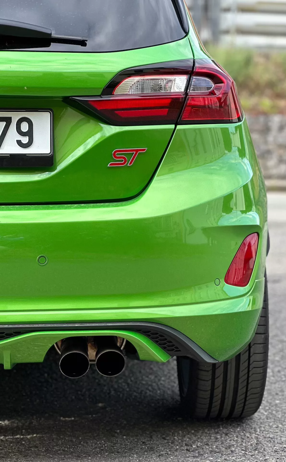 Vue rapprochée de l'arrière de la Ford Fiesta ST 2022 en finition métallique vert vif, mettant en avant les feux arrière LED, le double échappement chromé et le diffuseur arrière aérodynamique