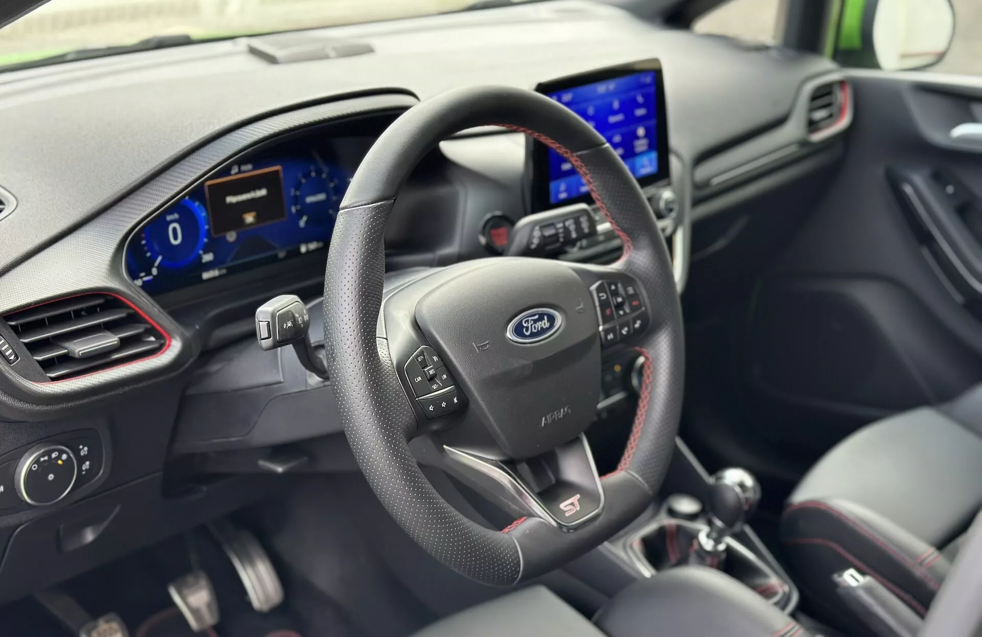 Intérieur de la Ford Fiesta 2022 du point de vue du conducteur, avec volant en cuir doté de boutons de commande, logo Ford, tableau de bord numérique et système d'infodivertissement moderne