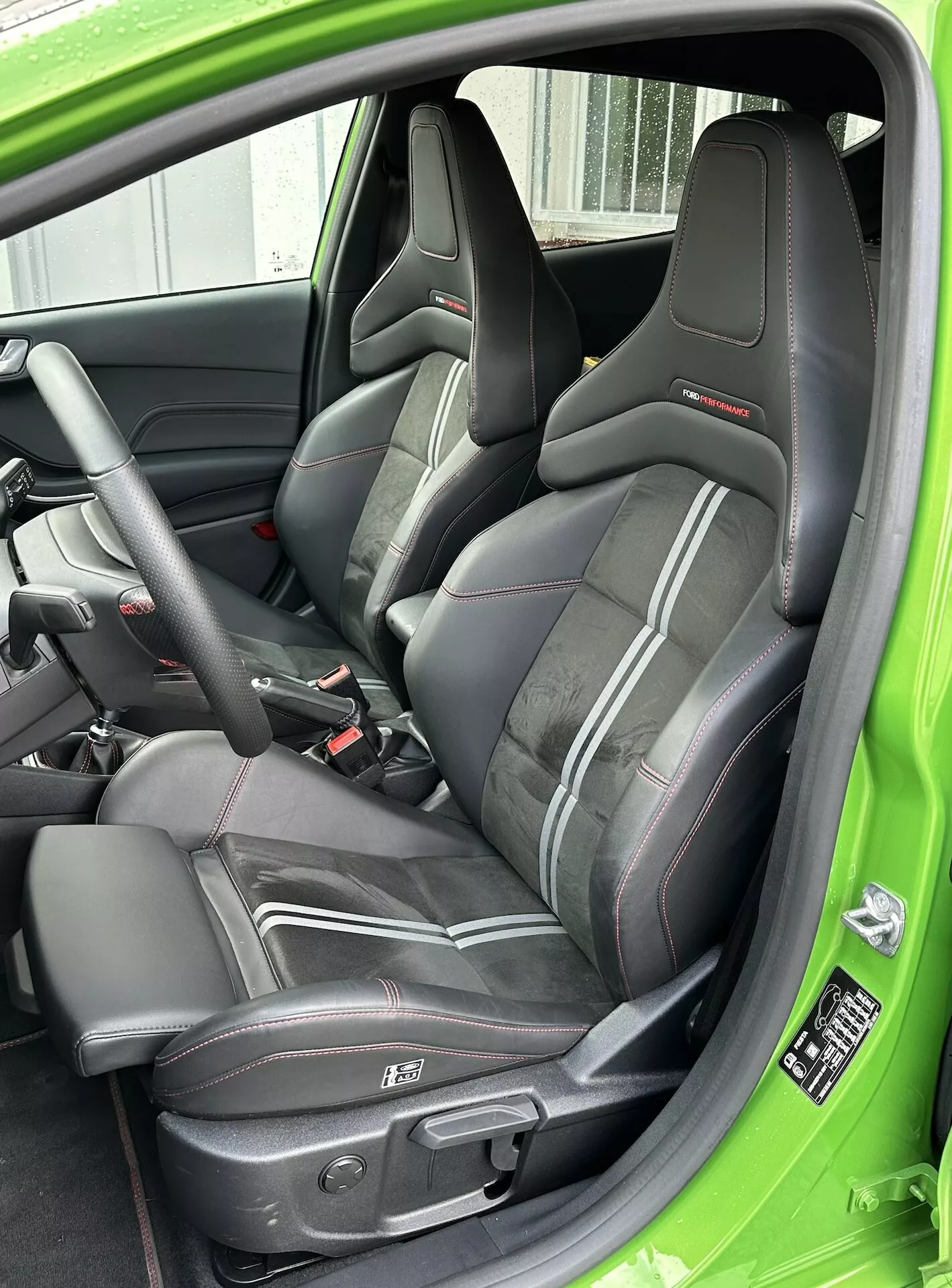 Vue rapprochée du siège conducteur sportif en cuir avec liseré rouge, ceinture de sécurité à trois points et commandes électriques du siège, accentuée par un revêtement intérieur vert de la Ford Fiesta 2022.