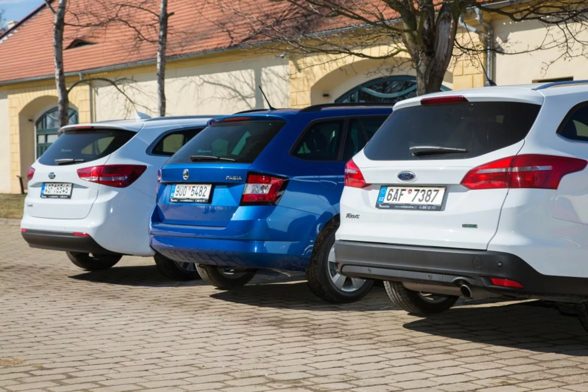 Une gamme de trois hatchbacks, y compris une Ford Focus blanche de 2011, garés perpendiculairement avec les extrémités arrière face à la caméra, montrant les feux arrières et les caractéristiques de conception arrière dans une zone de stationnement bien éclairée.