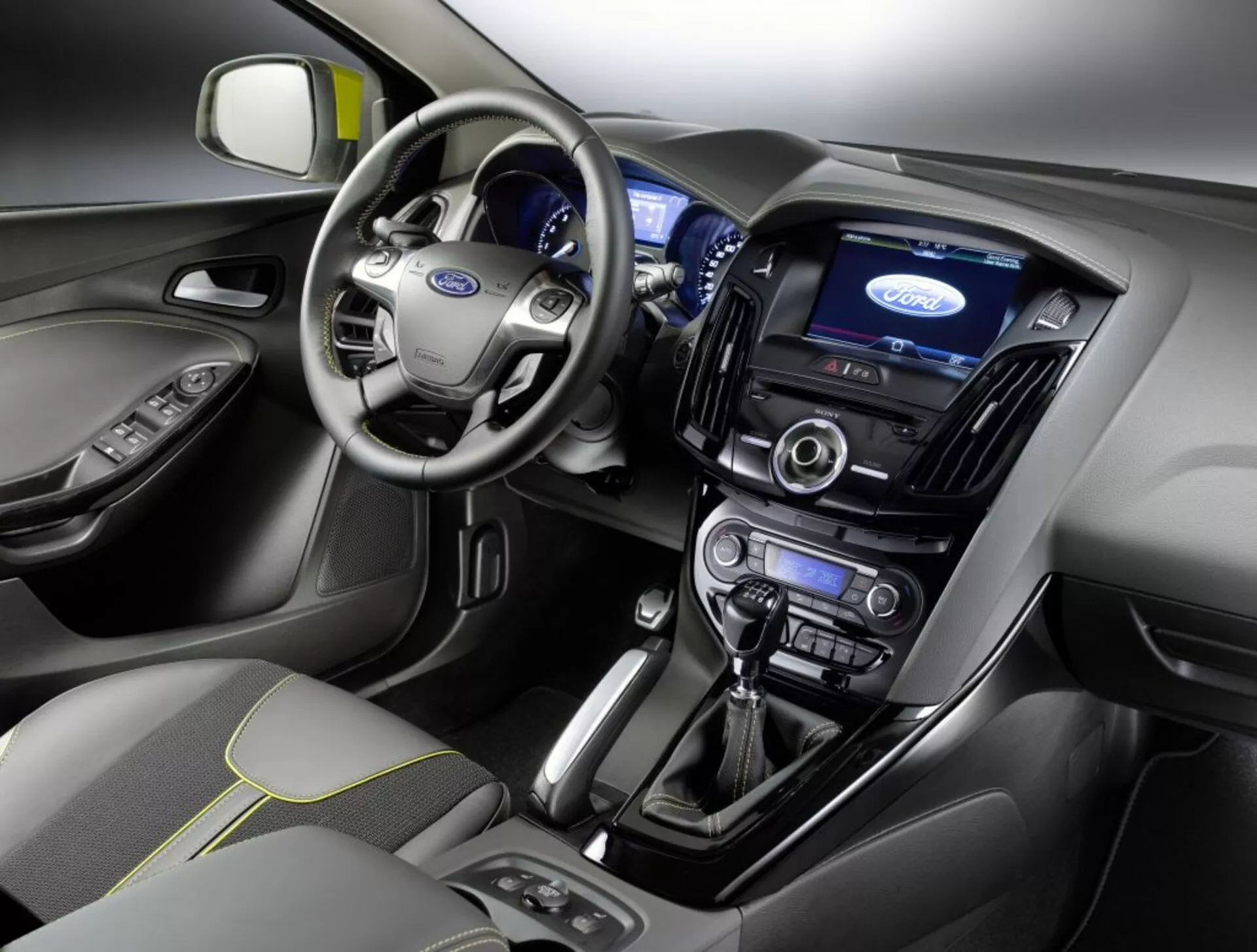 Vue intérieure d'une Ford Focus 2011 mettant en vedette le tableau de bord, l'espace conducteur, volant avec logo Ford, tableau de bord illuminé, écran tactile central d'infodivertissement, commandes de climatisation, système audio, levier de vitesse automatique et siège passager avant recouvert de tissu avec motif de couture