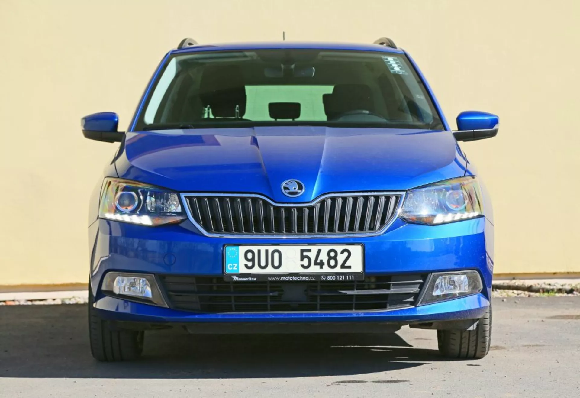 Vue de face d'un véhicule bleu Škoda présentant l'emblème de la marque sur la grille chromée, des phares à lentilles claires et des feux de brouillard dans un logement noir, avec une grille inférieure détaillée et un design de capot sculpté.