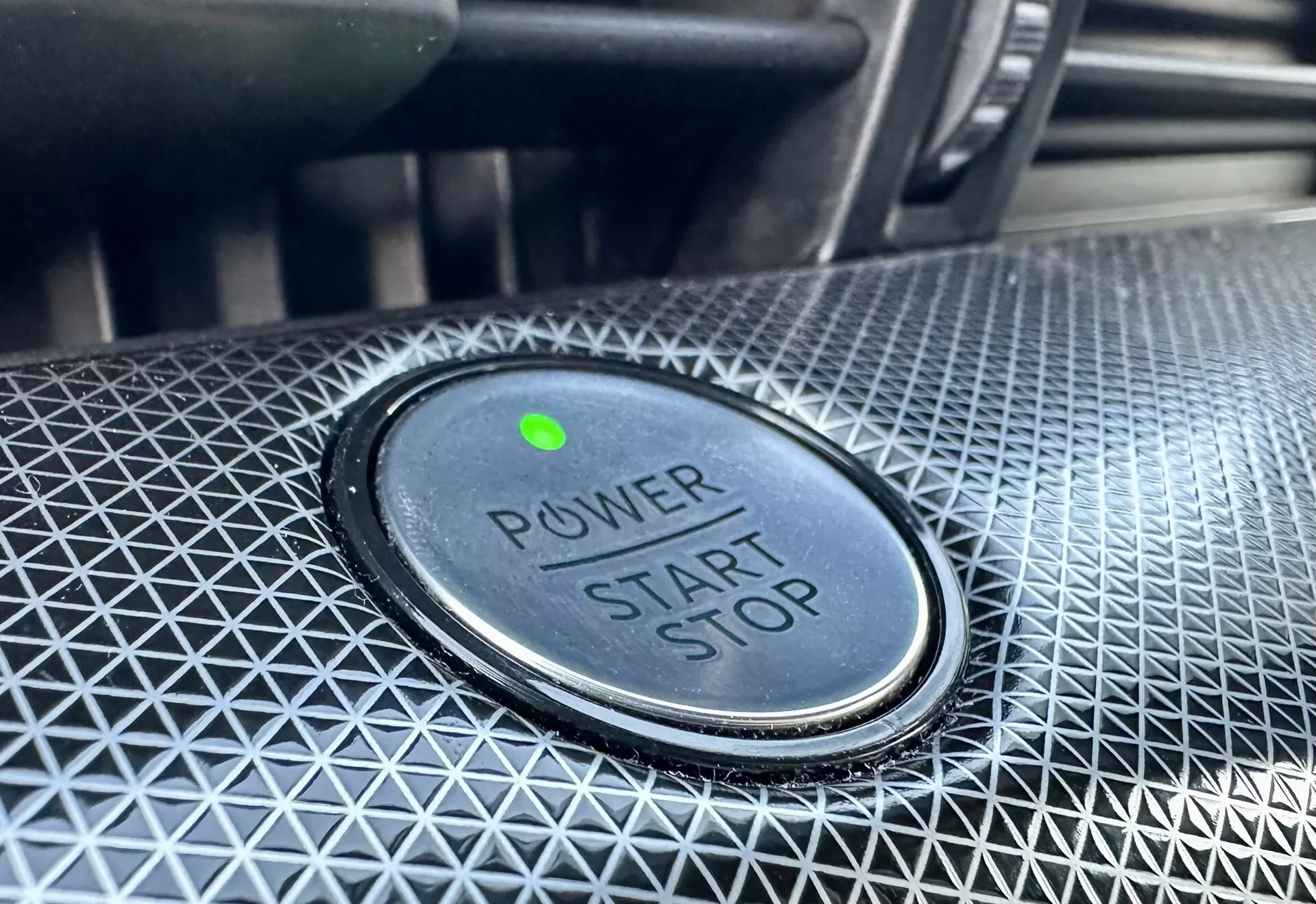 Vue rapprochée du bouton de démarrage/arrêt dans une Ford Mustang-Mach-E 2020, avec le texte 'POWER START STOP', voyant lumineux vert et conception texturée environnante