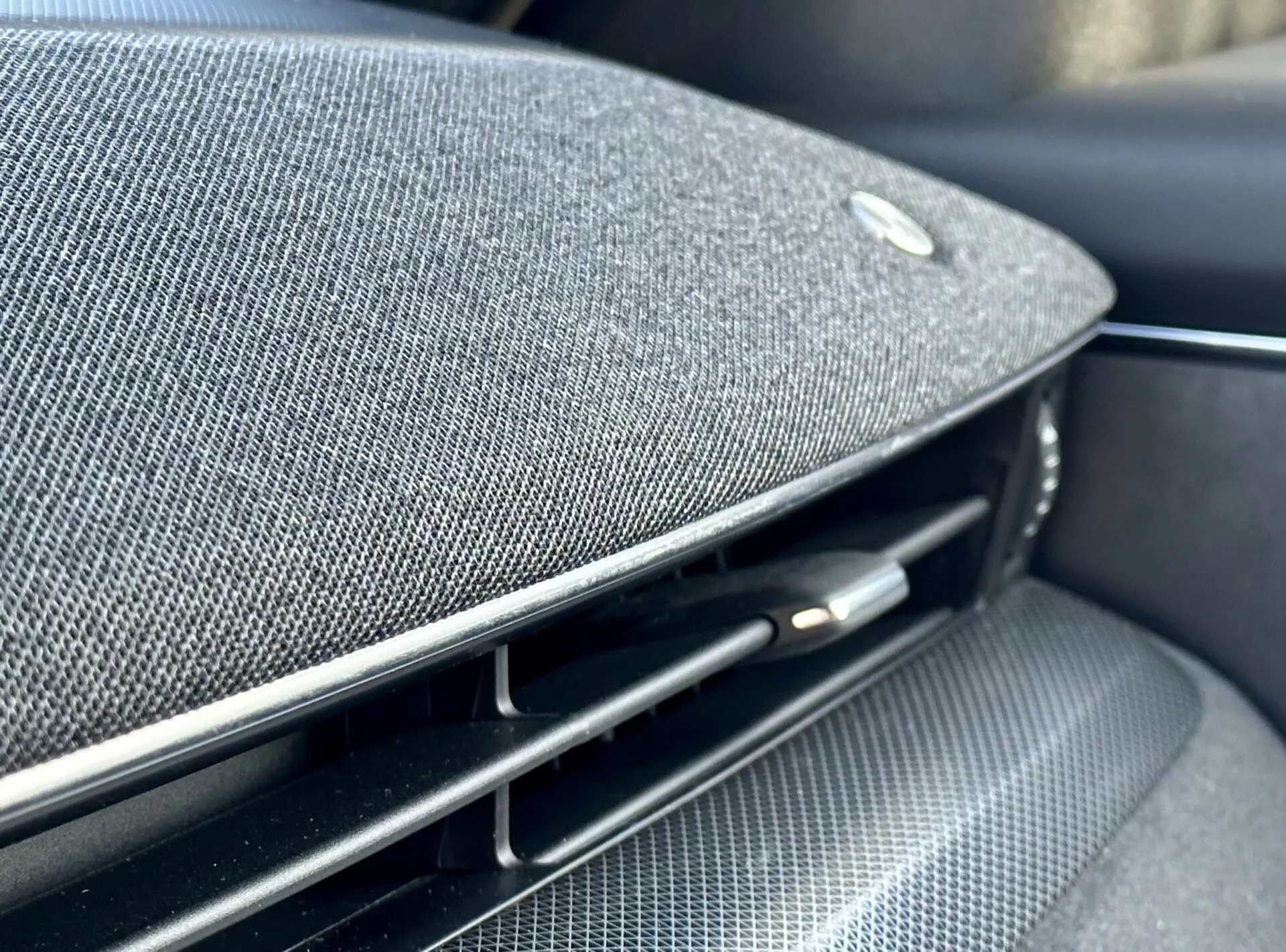Vue rapprochée à l'intérieur de la Ford Mustang Mach-E 2020 montrant une partie du tableau de bord ou du panneau de porte avec une grille de haut-parleur en tissu haut de gamme intégrée, un emblème suggérant un partenariat avec un fabricant d'équipements audio haut de gamme, à côté d'une grille d'aération noire brillante