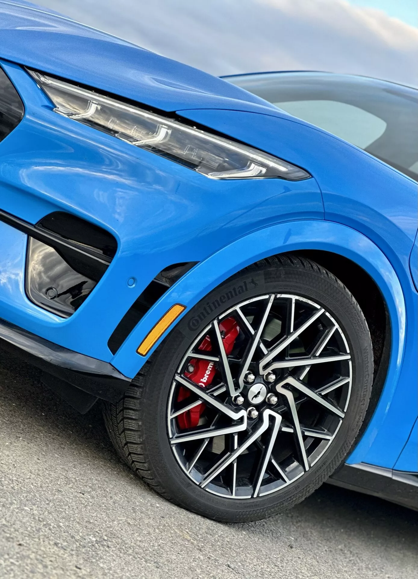 Gros plan détaillé sur le côté avant gauche du Ford Mustang Mach-E 2020, mettant en évidence la roue en alliage avec étrier de frein rouge, l'aile avant élégante avec une ouïe de refroidissement, vue partielle du phare LED moderne, couleur de carrosserie bleue sportive et améliorations du trim extérieur