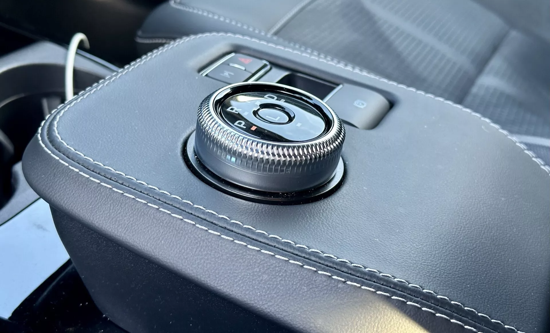 Vue rapprochée de l'intérieur de la Ford Mustang Mach-E 2020 avec un contrôle rotatif sur la console centrale sur une surface enveloppée dans du cuir avec des coutures blanches, offrant une interface ergonomique pour le système d'infodivertissement