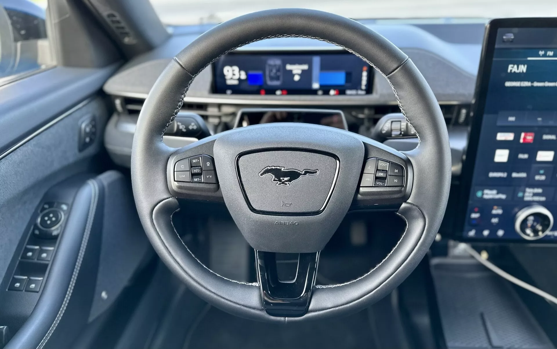 Vue intérieure d'une Ford Mustang-Mach-E 2020 du point de vue du conducteur, présentant un volant à trois branches avec commandes, un tableau de bord numérique et un grand écran tactile d'infodivertissement