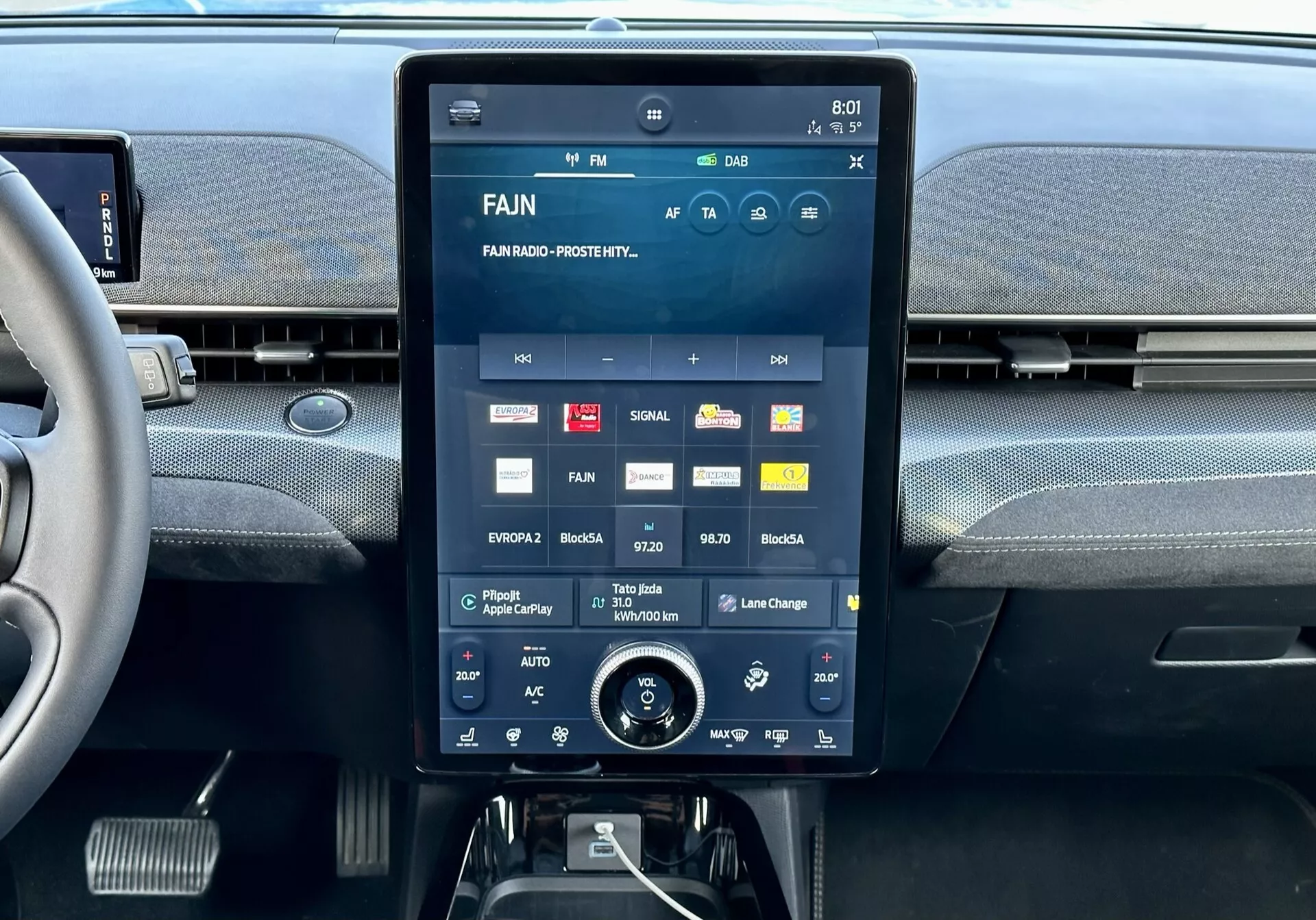 Console centrale intérieure de la Ford Mustang Mach-E 2020 avec un grand écran tactile affichant l'interface multimédia avec applications et réglages, aérations intégrées au-dessus, et un bouton rotatif de contrôle de climat en dessous.